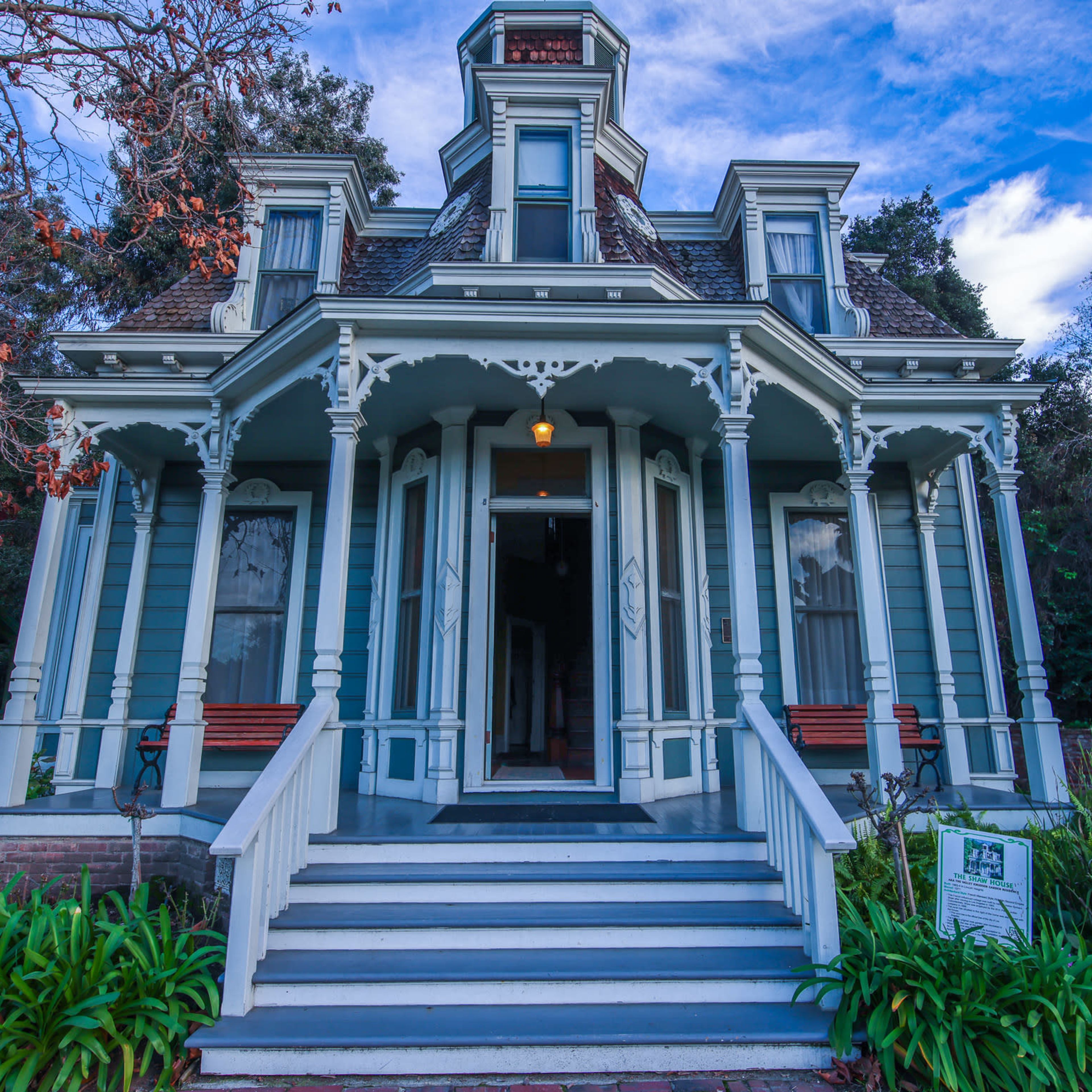 A large, Victorian-style house with a prominent front porch and decorative trim, surrounded by greenery.