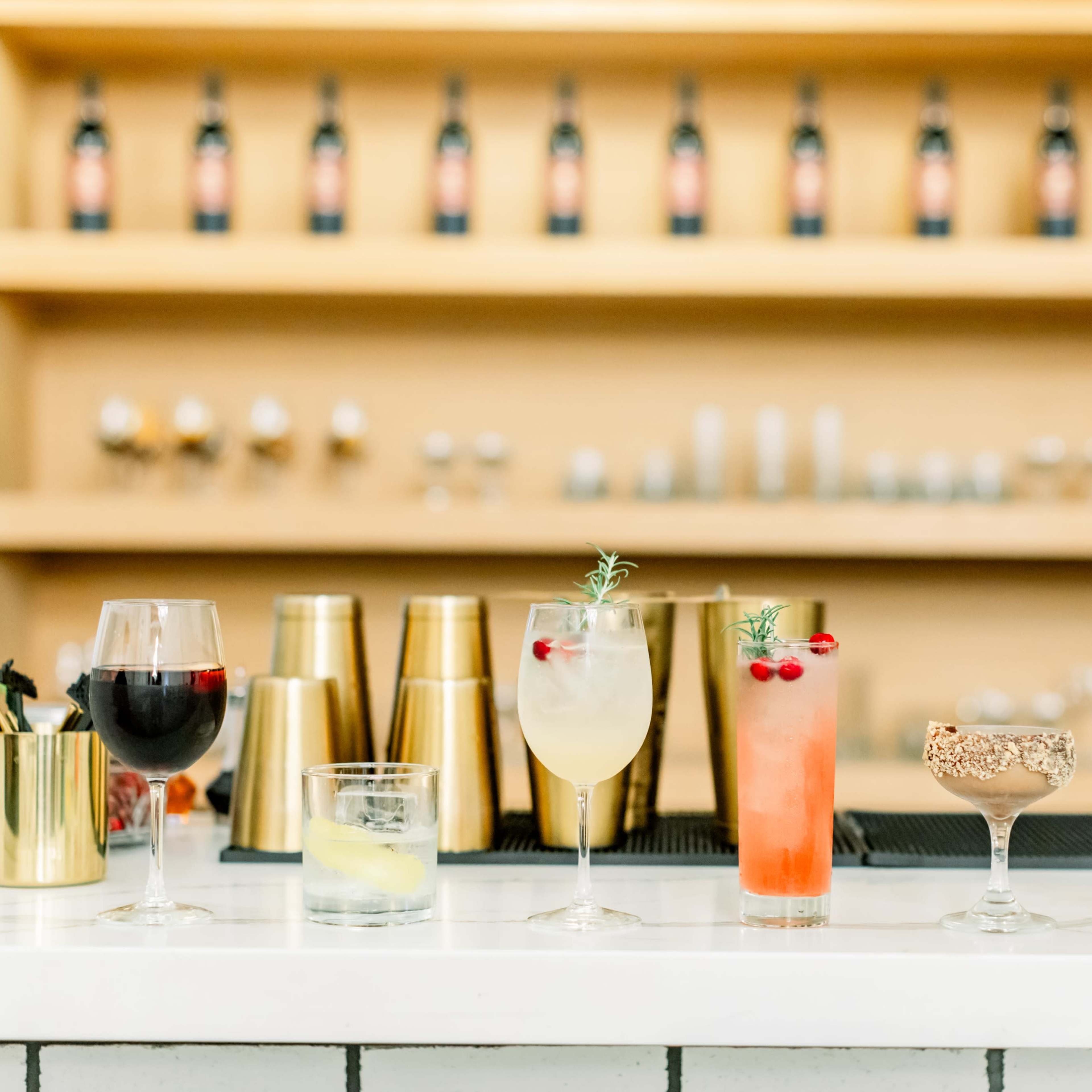 A selection of eight cocktails arranged on a bar counter, with various glassware and garnishes in front of shelves filled with bottles.