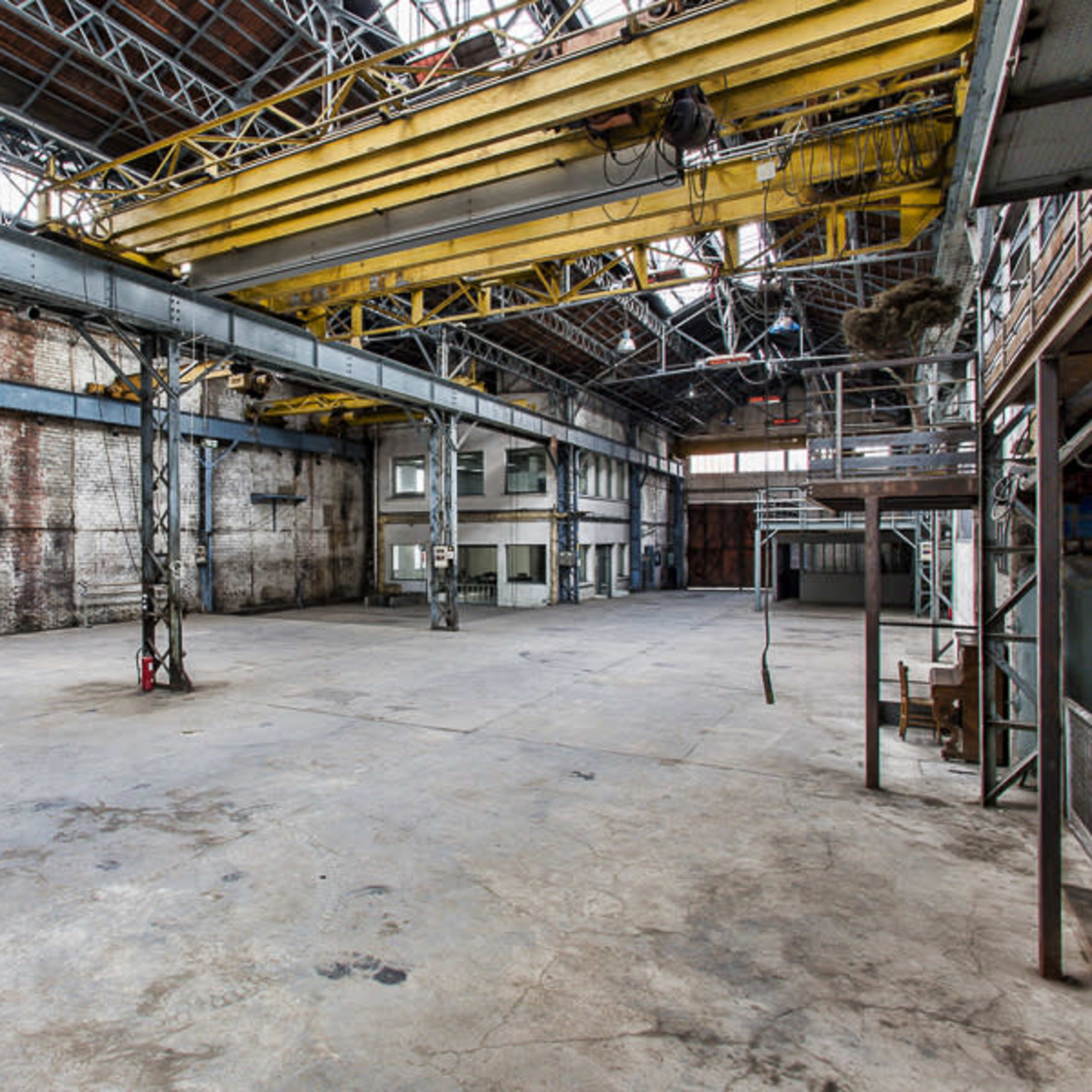 A large, empty industrial warehouse with exposed brick walls and high ceilings supported by metal beams.