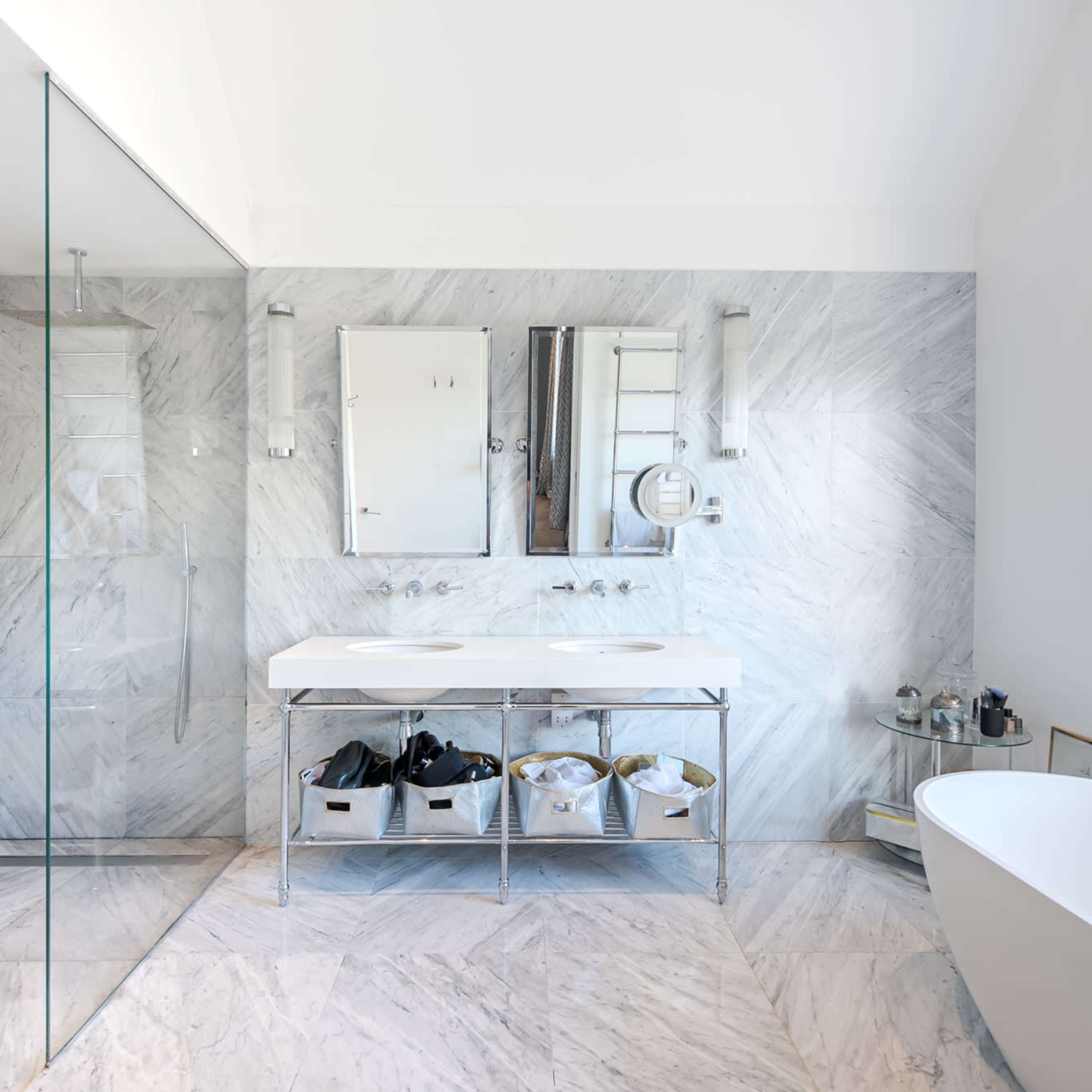 A modern bathroom featuring a glass shower enclosure, a double sink vanity with storage underneath, and a freestanding bathtub next to a large window.