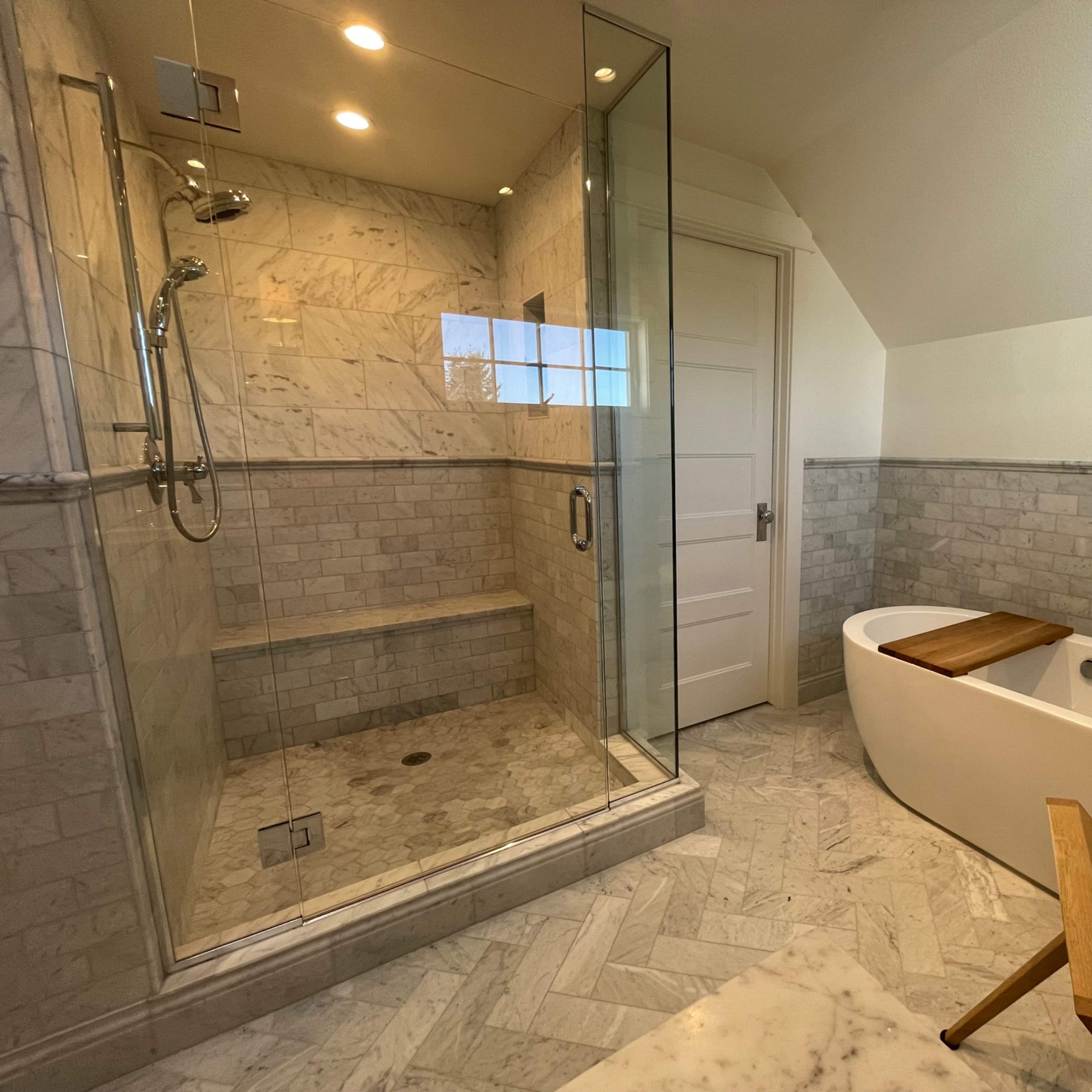 A modern bathroom featuring a glass-enclosed shower, a freestanding bathtub, and marble tile throughout.