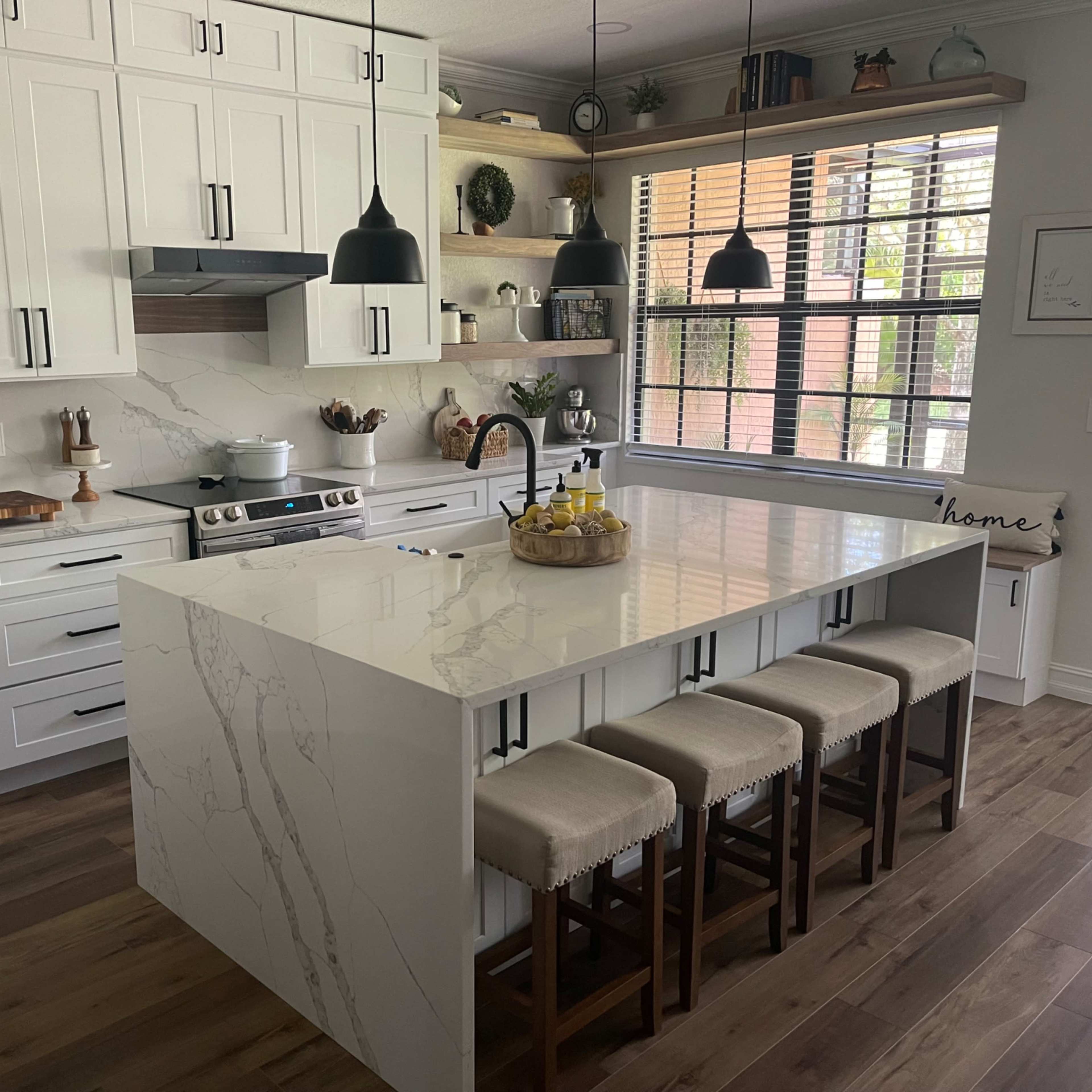 A modern kitchen featuring white cabinetry, a large island with a marble countertop, and four wooden stools.