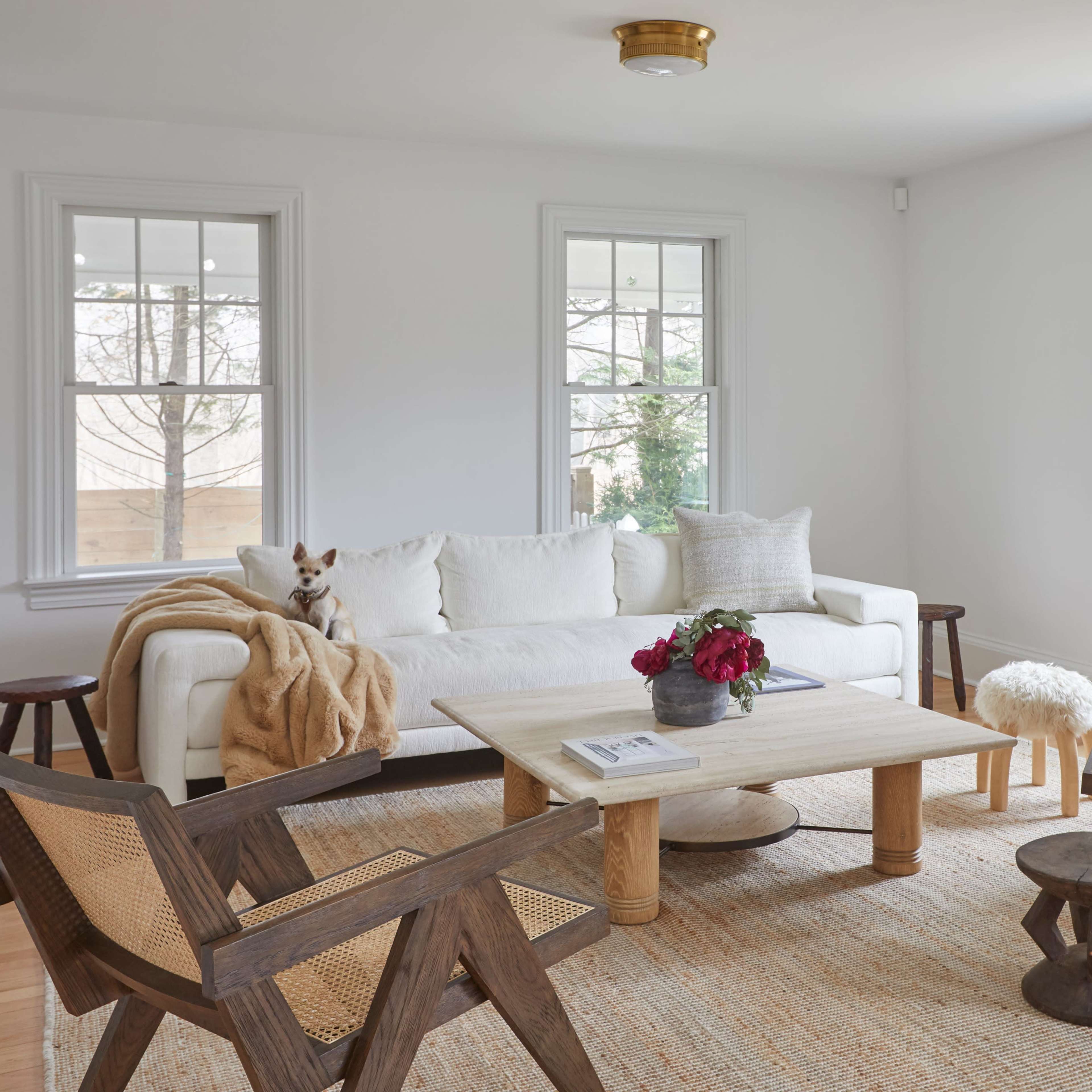 A bright living room with a white sofa, two wooden chairs, a round coffee table, and a woven rug.