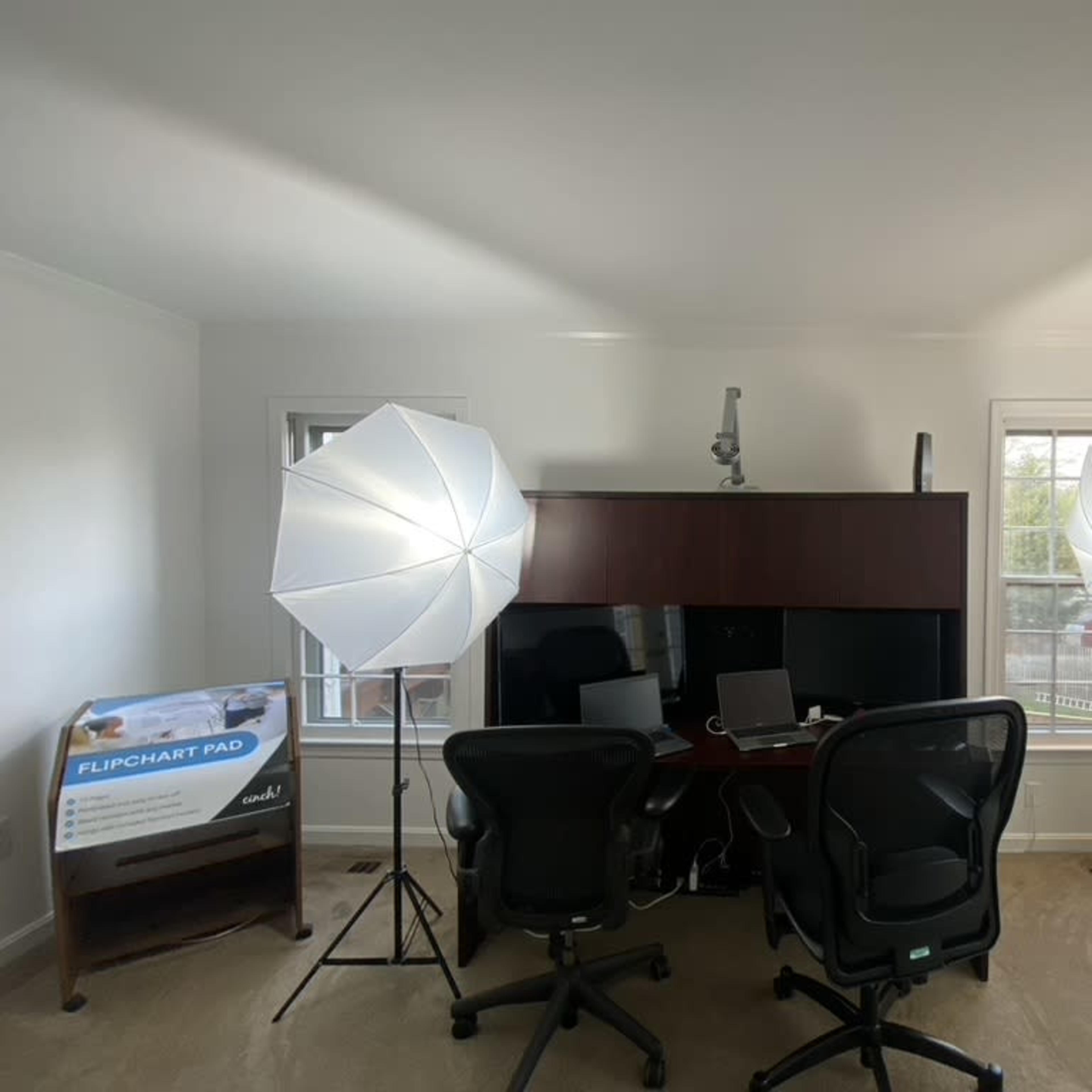A well-lit office space featuring two large softbox lights, a dark wooden desk with a computer, and a flipchart pad in the corner.