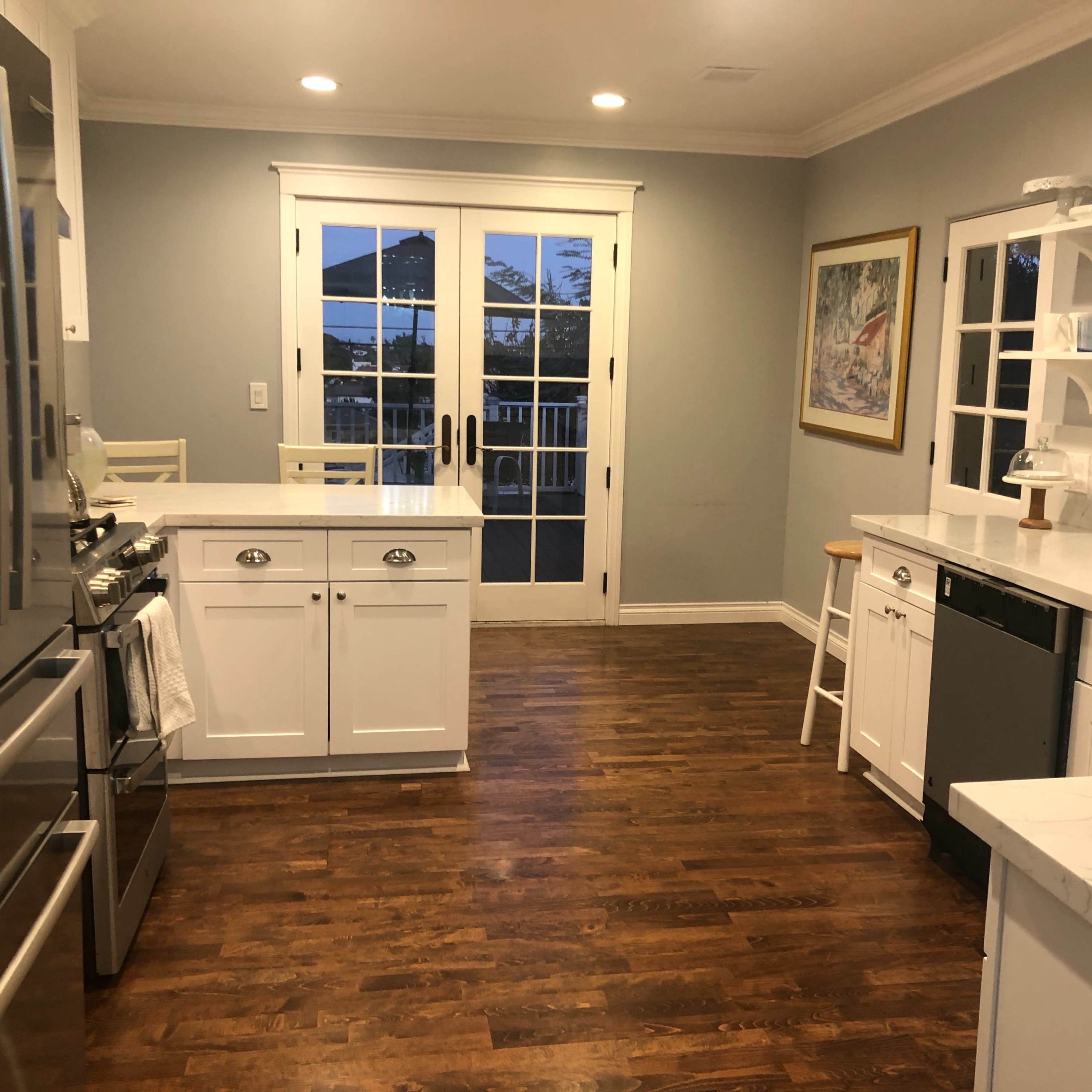 The kitchen features stainless steel appliances, white cabinetry, and a view through double doors leading outside.