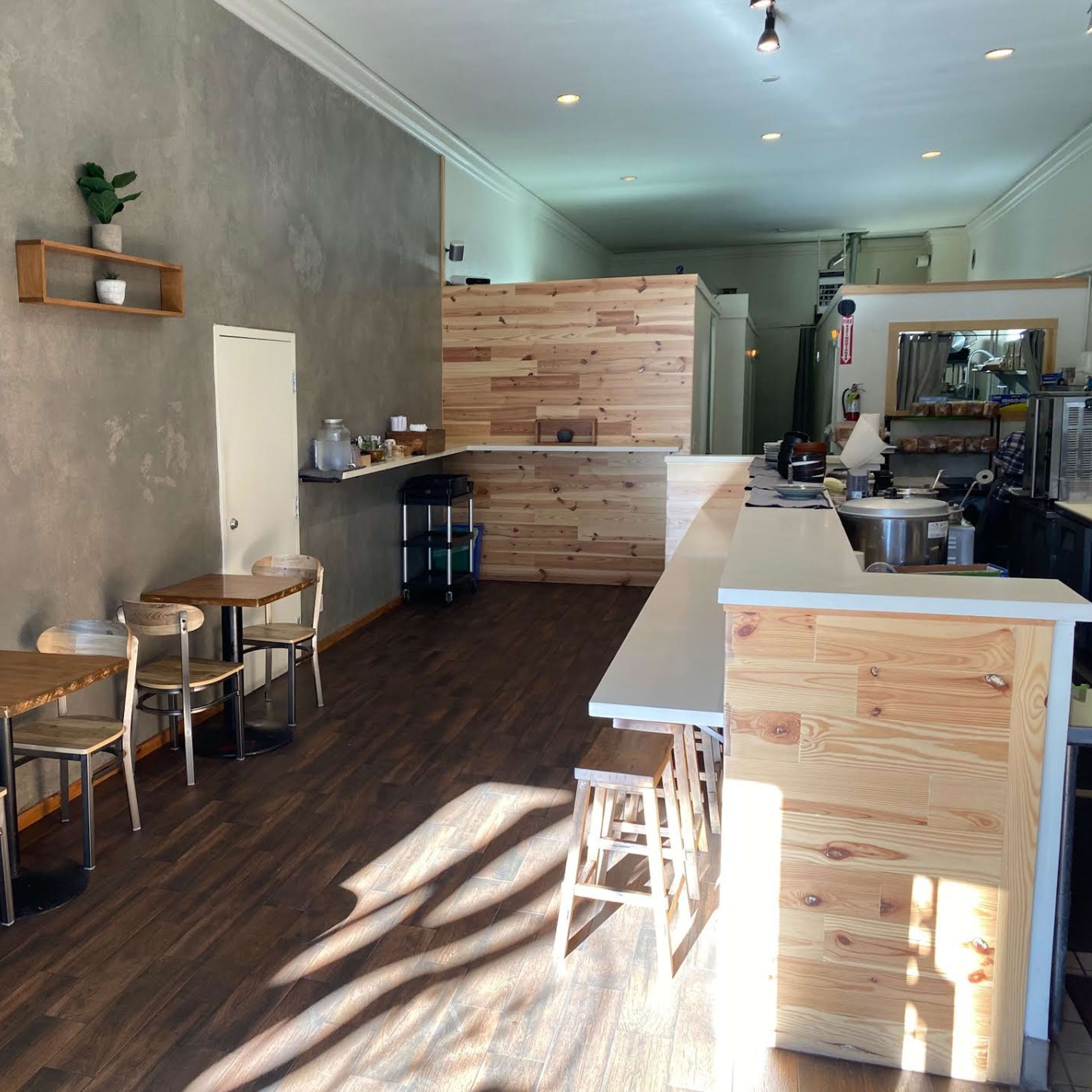 A minimalist café interior with wooden furniture, a simple counter, and a few potted plants on the walls.