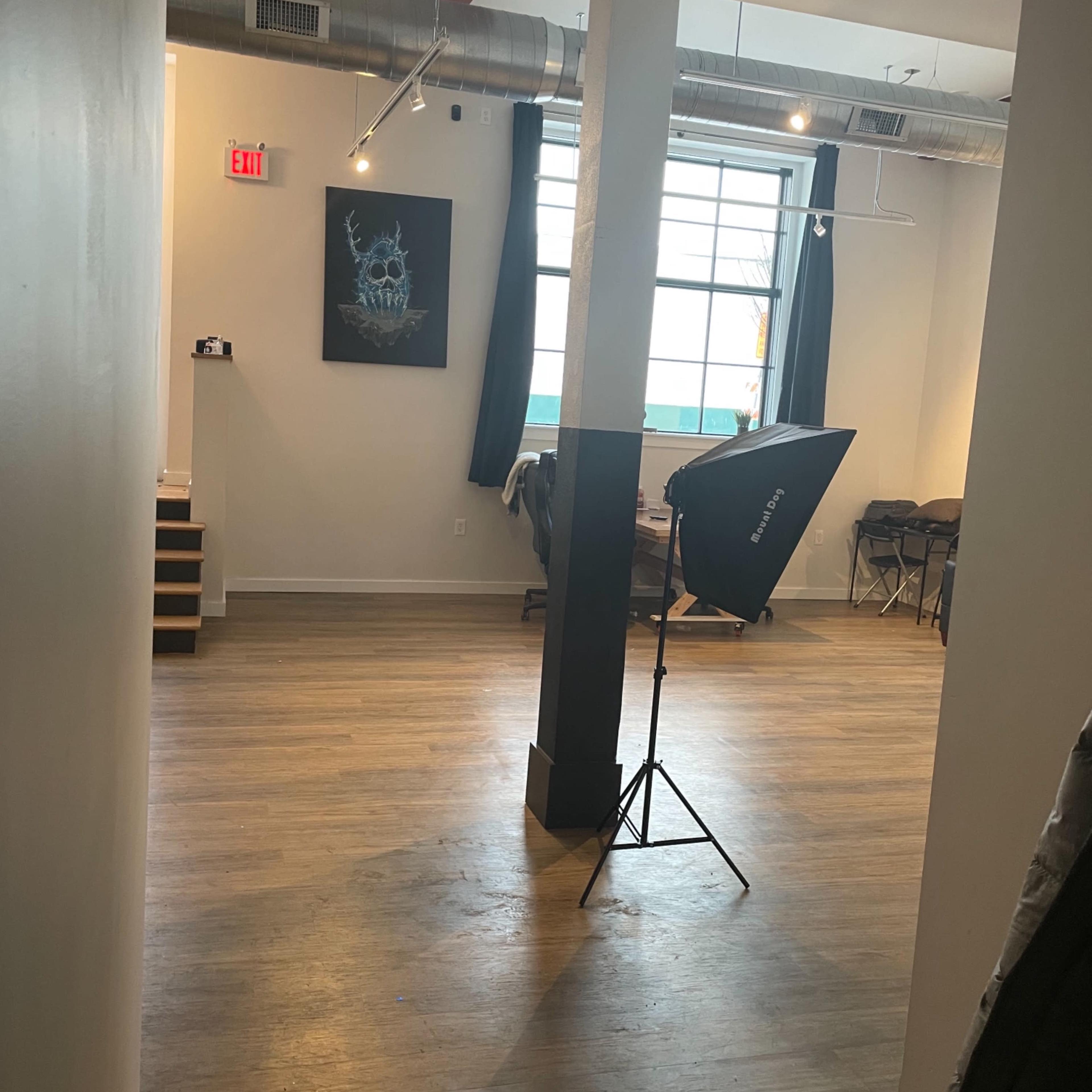 An interior space with a large window, a wall art piece, and a photography light stand set up on wooden flooring.