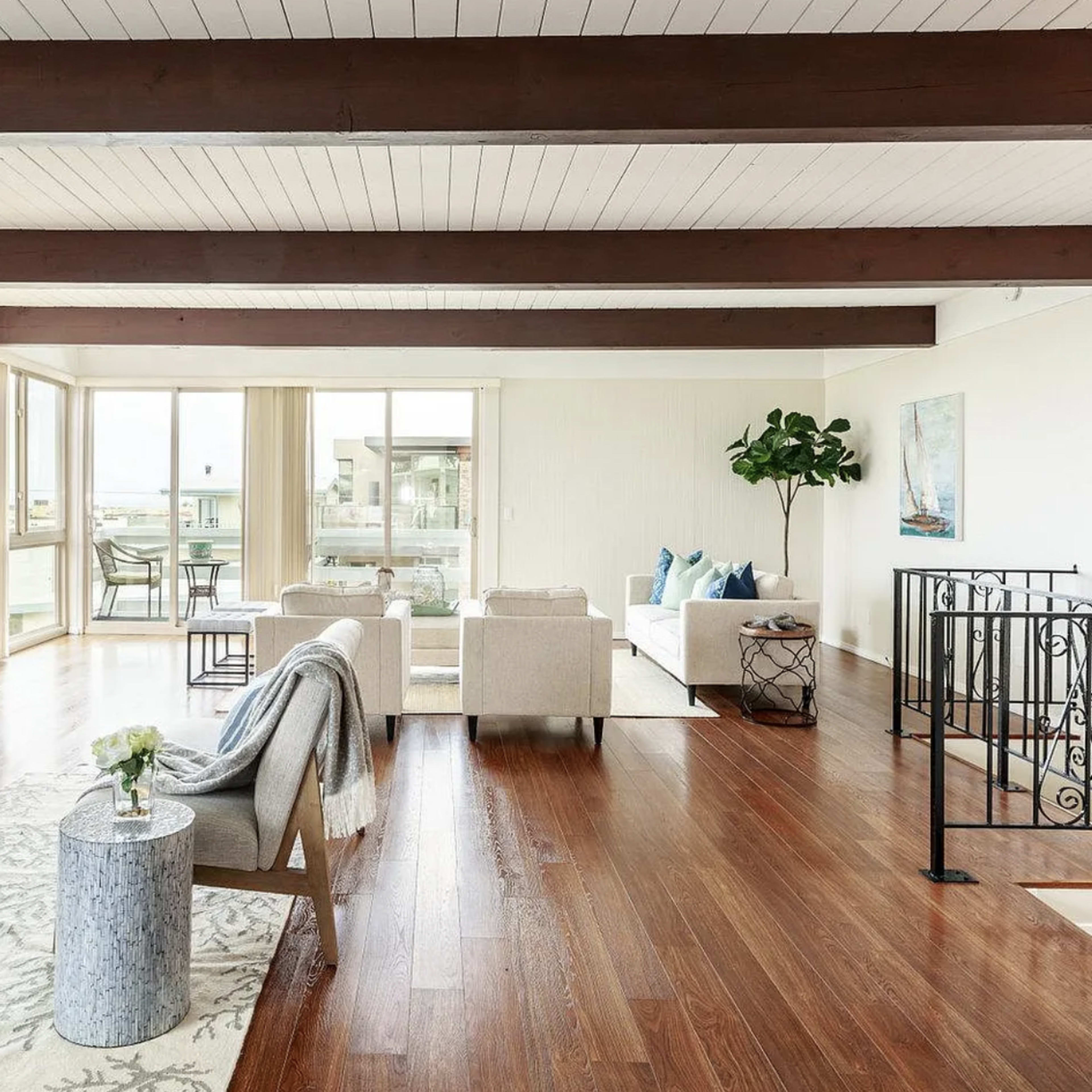 A spacious living room features large windows, wooden beams, and modern furniture arranged around a decorative table.