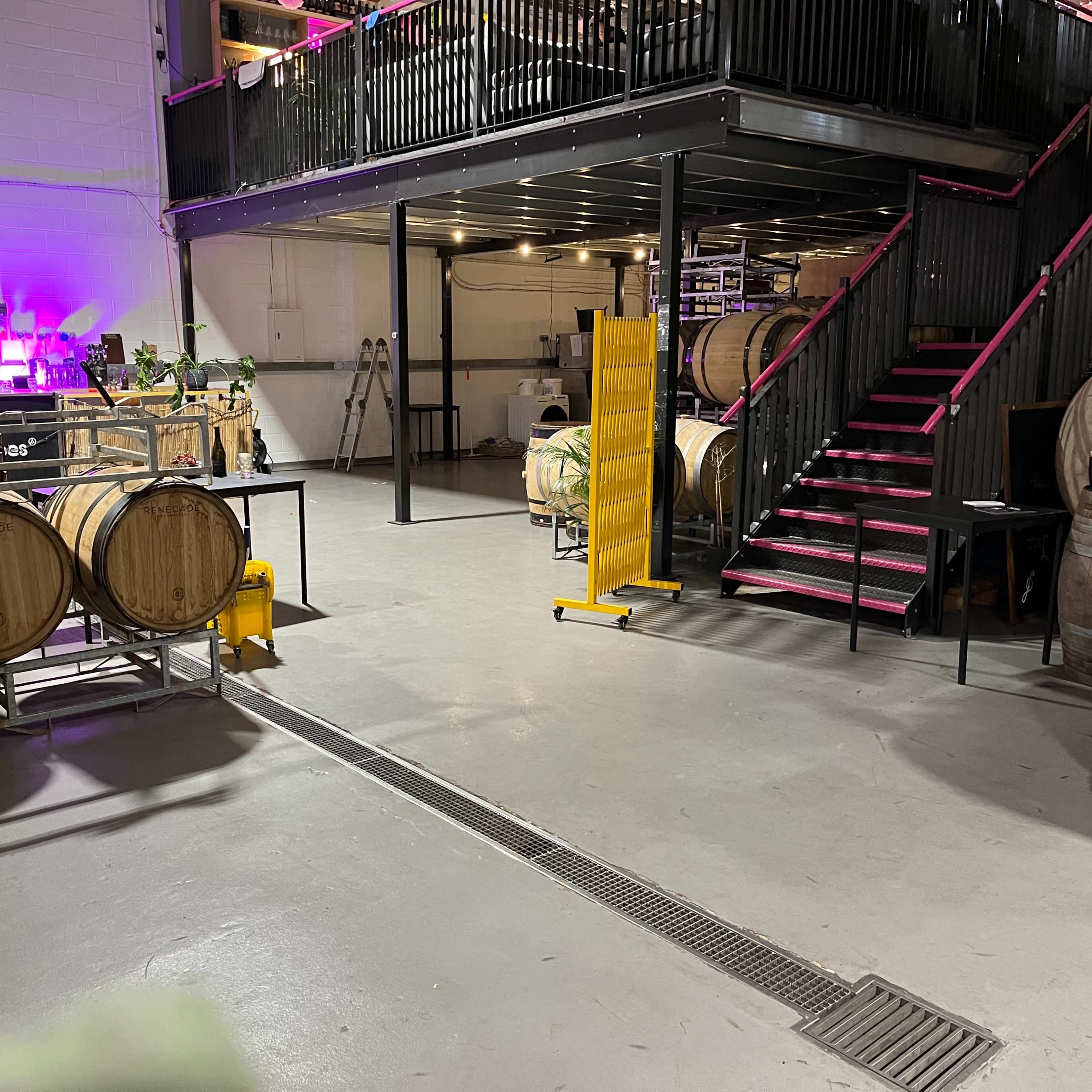 A spacious industrial area with wooden barrels and a staircase leading to a lofted section.
