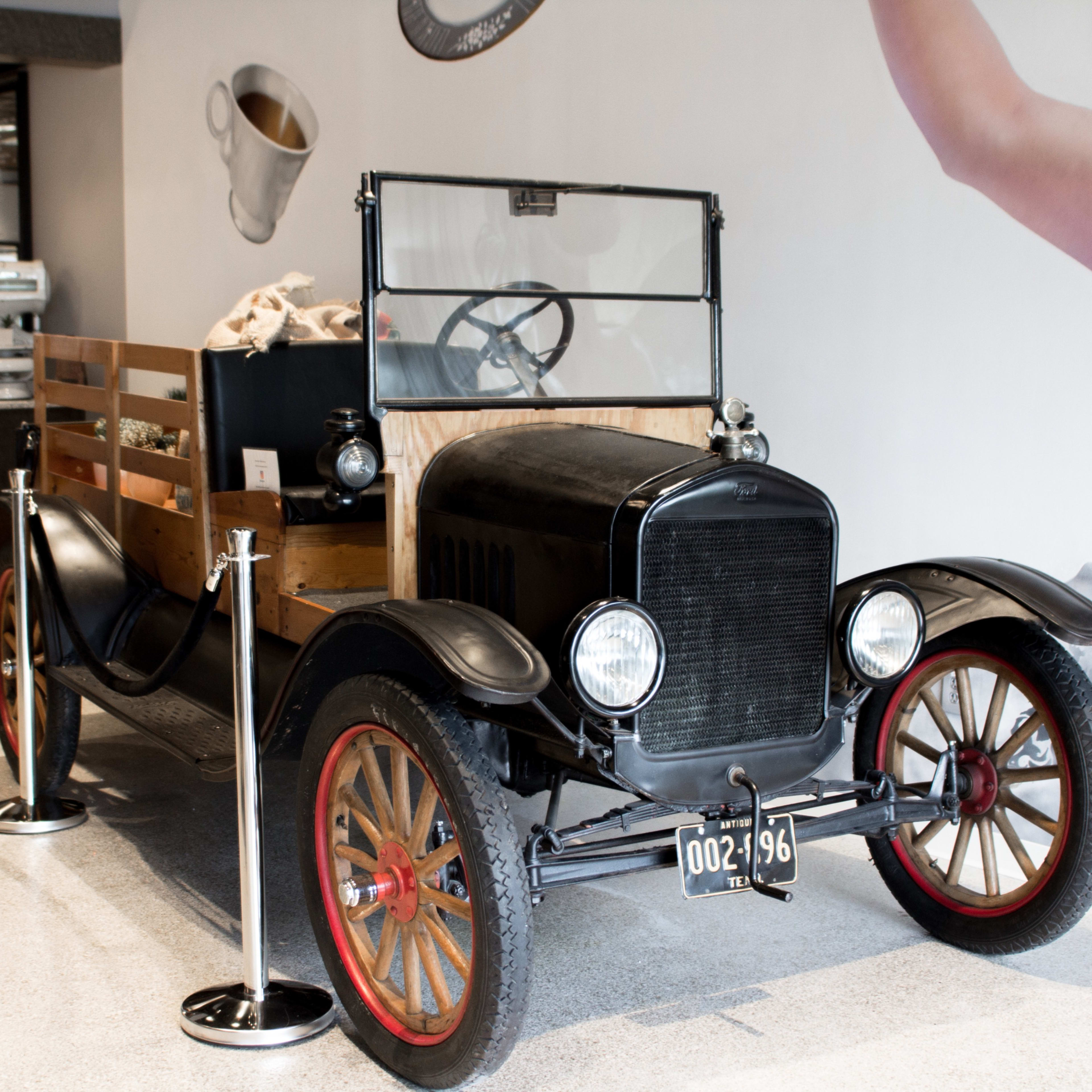 An antique black pickup truck with wooden sides is displayed inside a modern café.