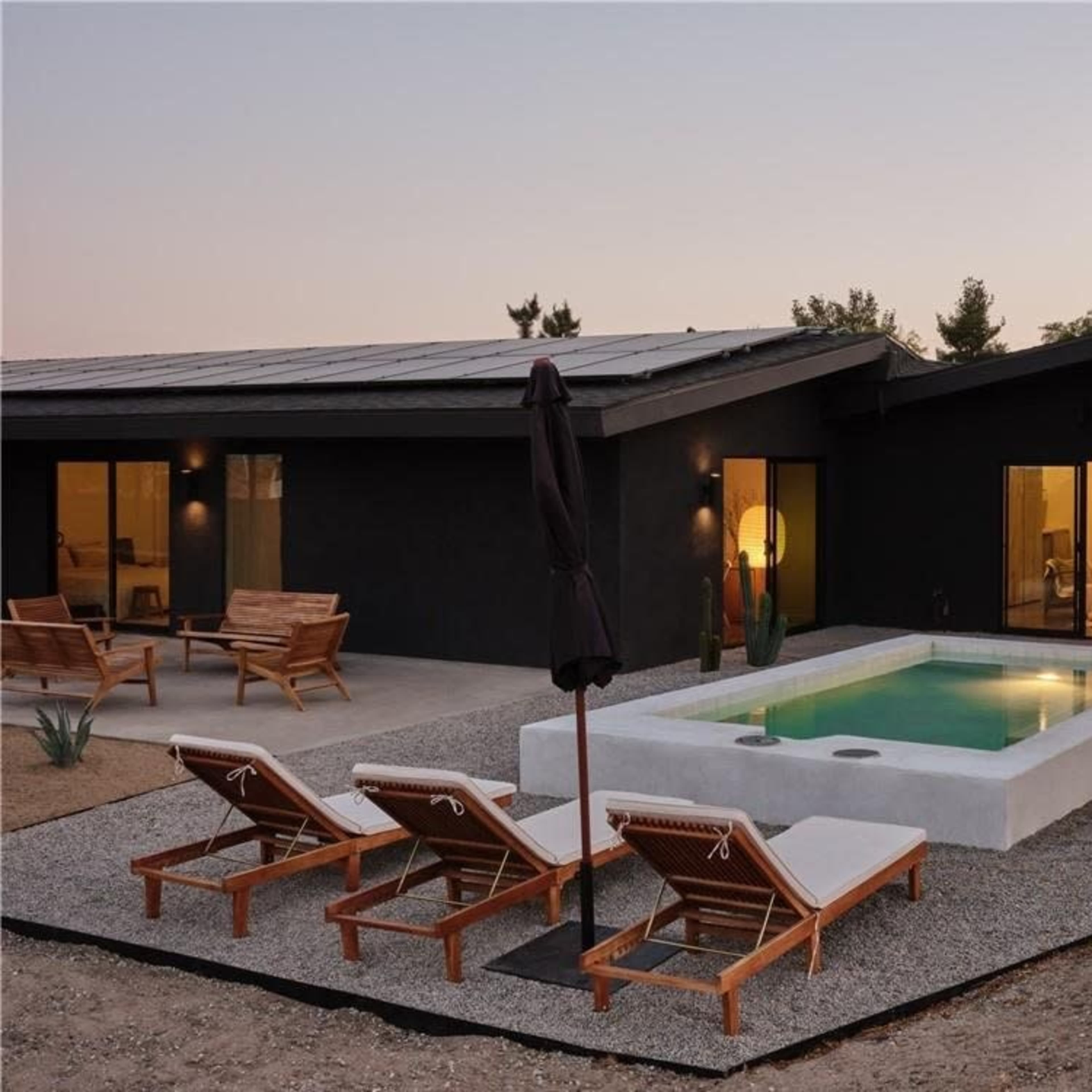 A modern house with a rectangular pool surrounded by lounge chairs on a gravel patio.
