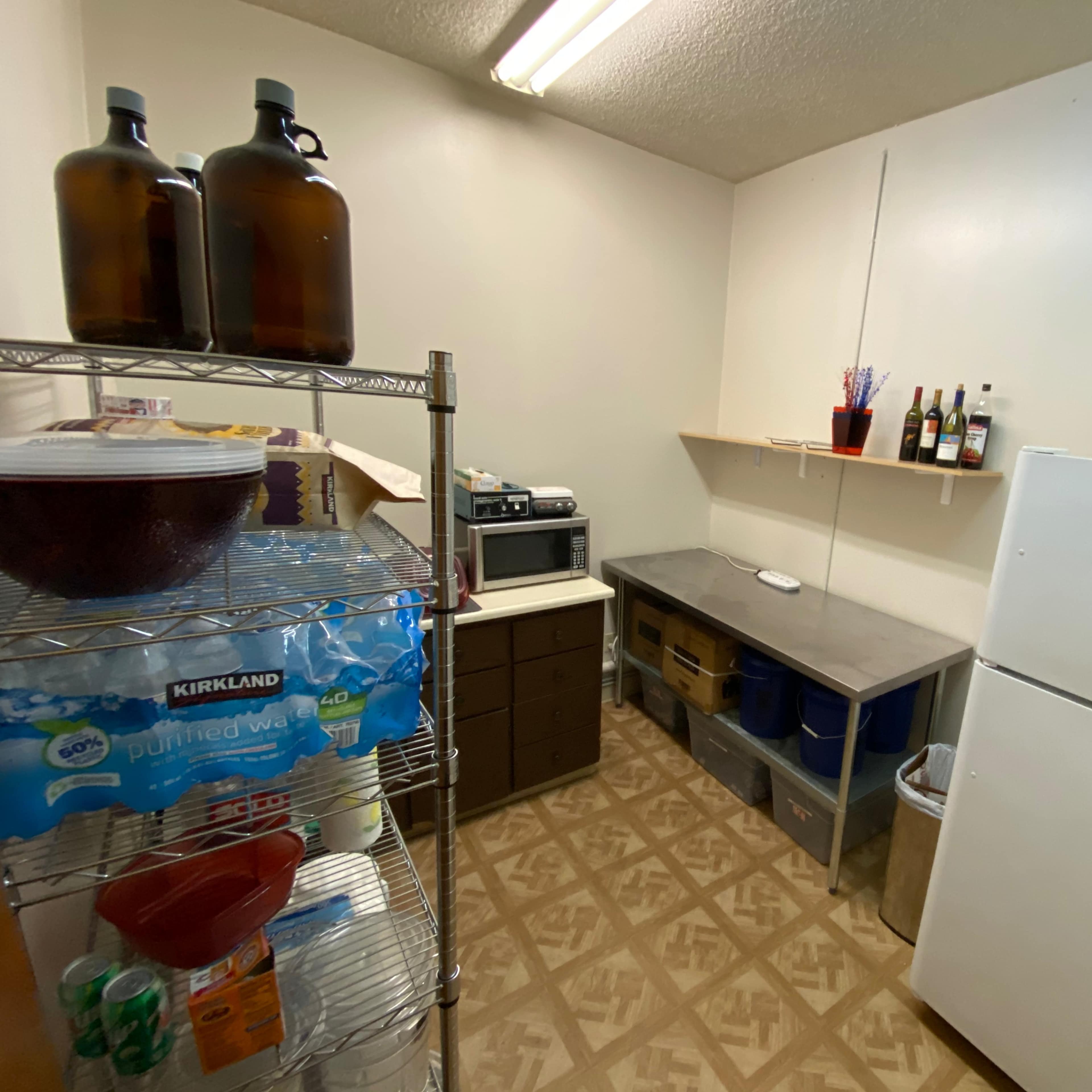 A small, organized kitchenette with shelves holding food items, a microwave, a countertop, and a refrigerator.