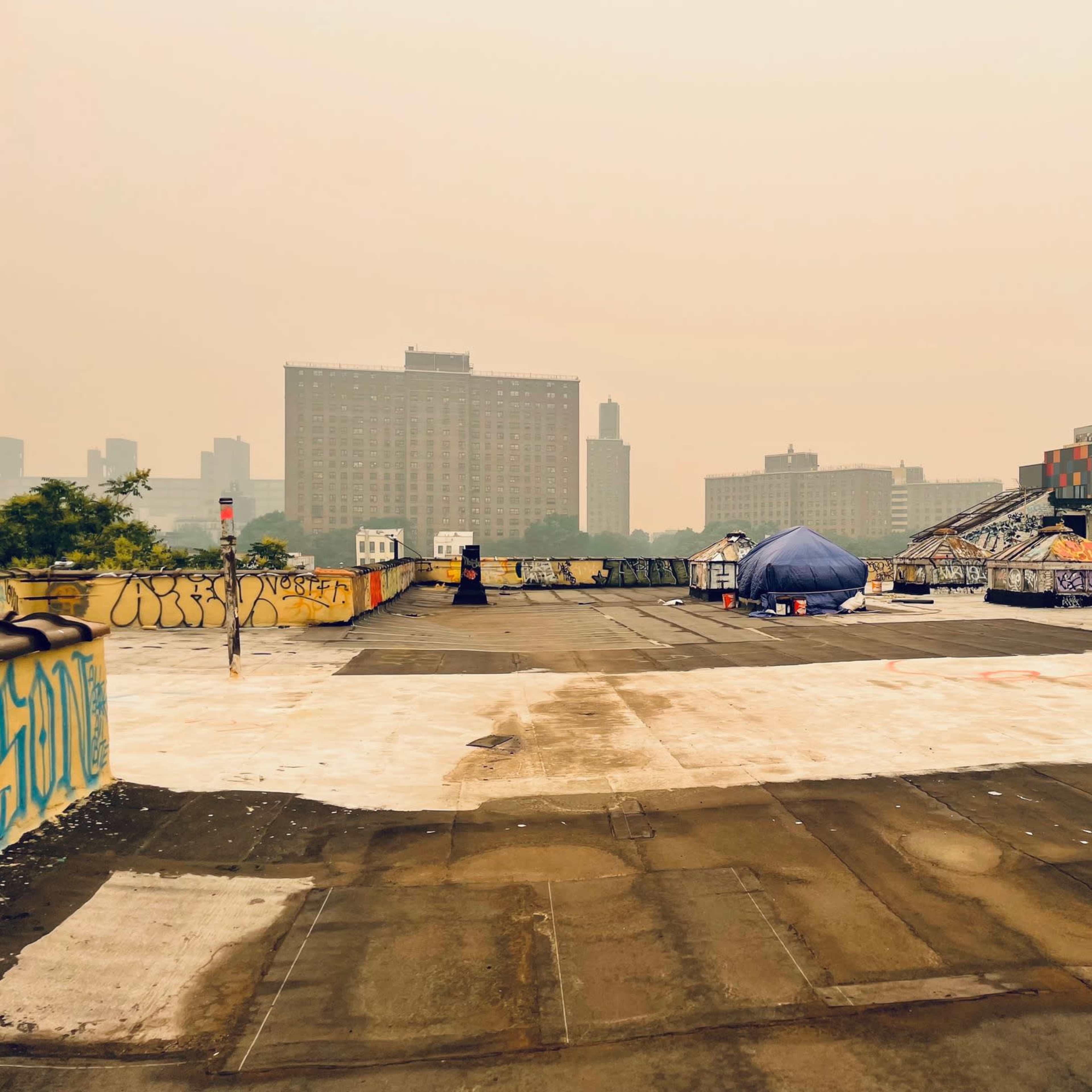 A rooftop scene features scattered tents and graffiti against a backdrop of tall buildings shrouded in a hazy atmosphere.