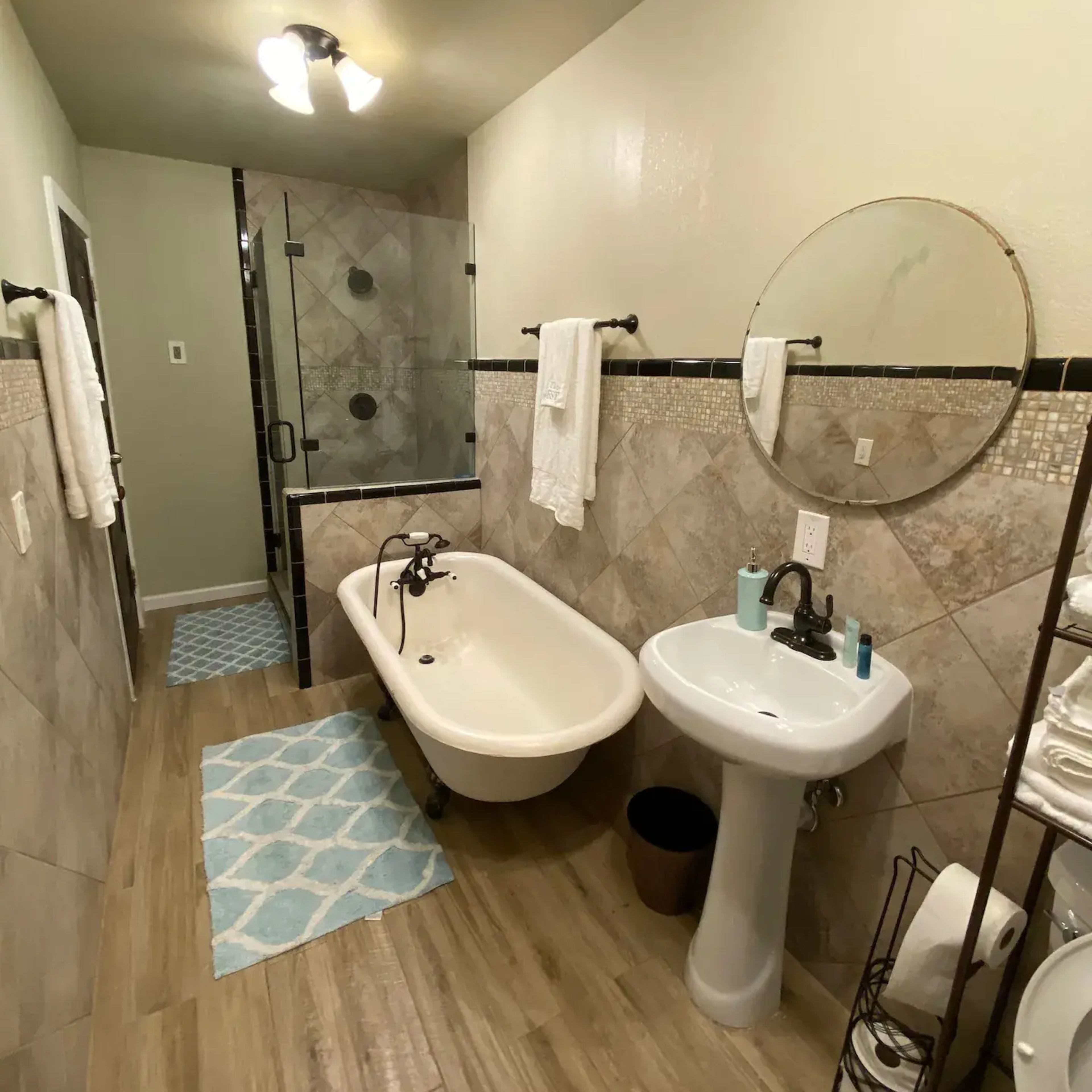 A bathroom featuring a freestanding bathtub, a glass shower enclosure, a pedestal sink, and tiled walls and floors.
