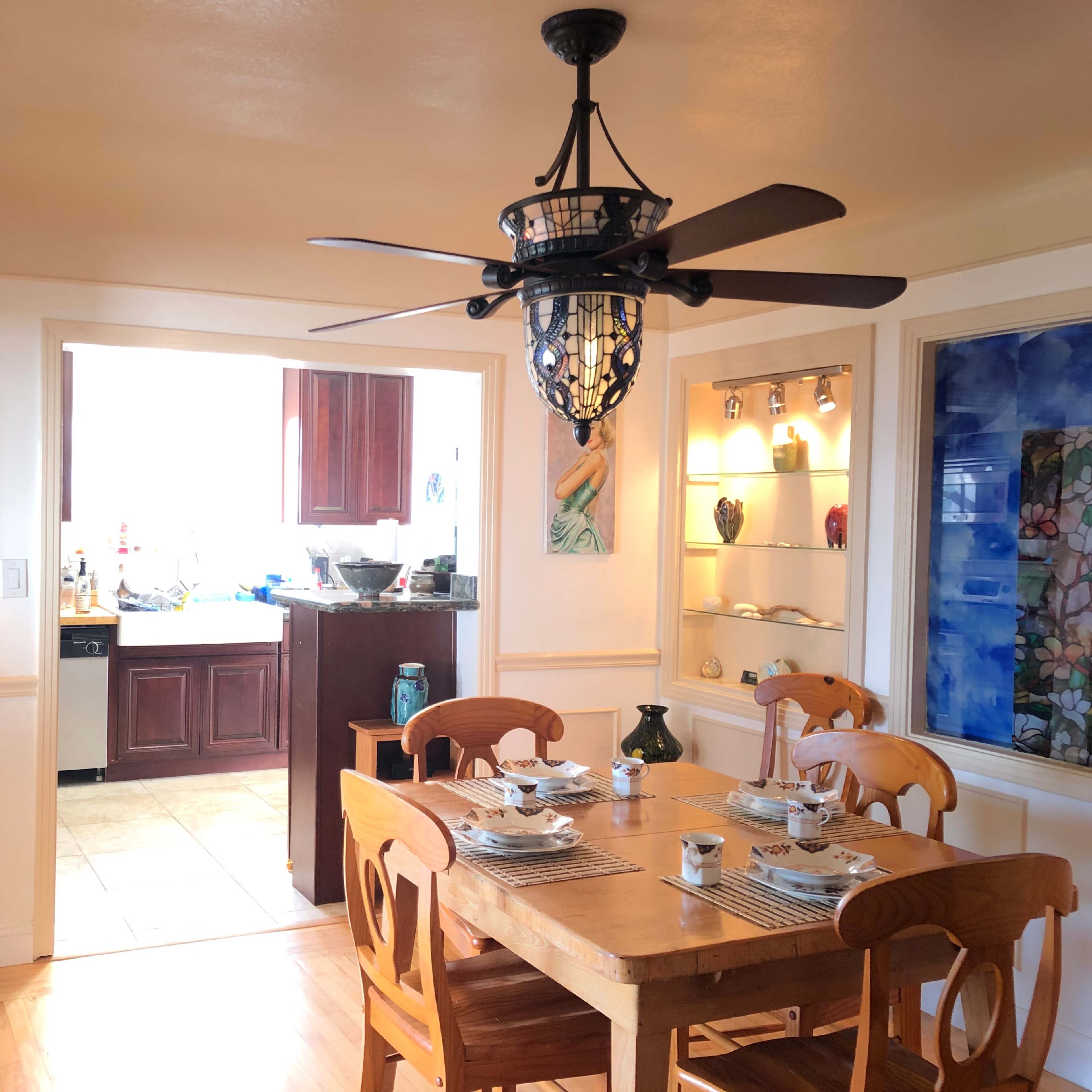 A dining area features a wooden table set with dishes and a ceiling fan, with a kitchen visible in the background.