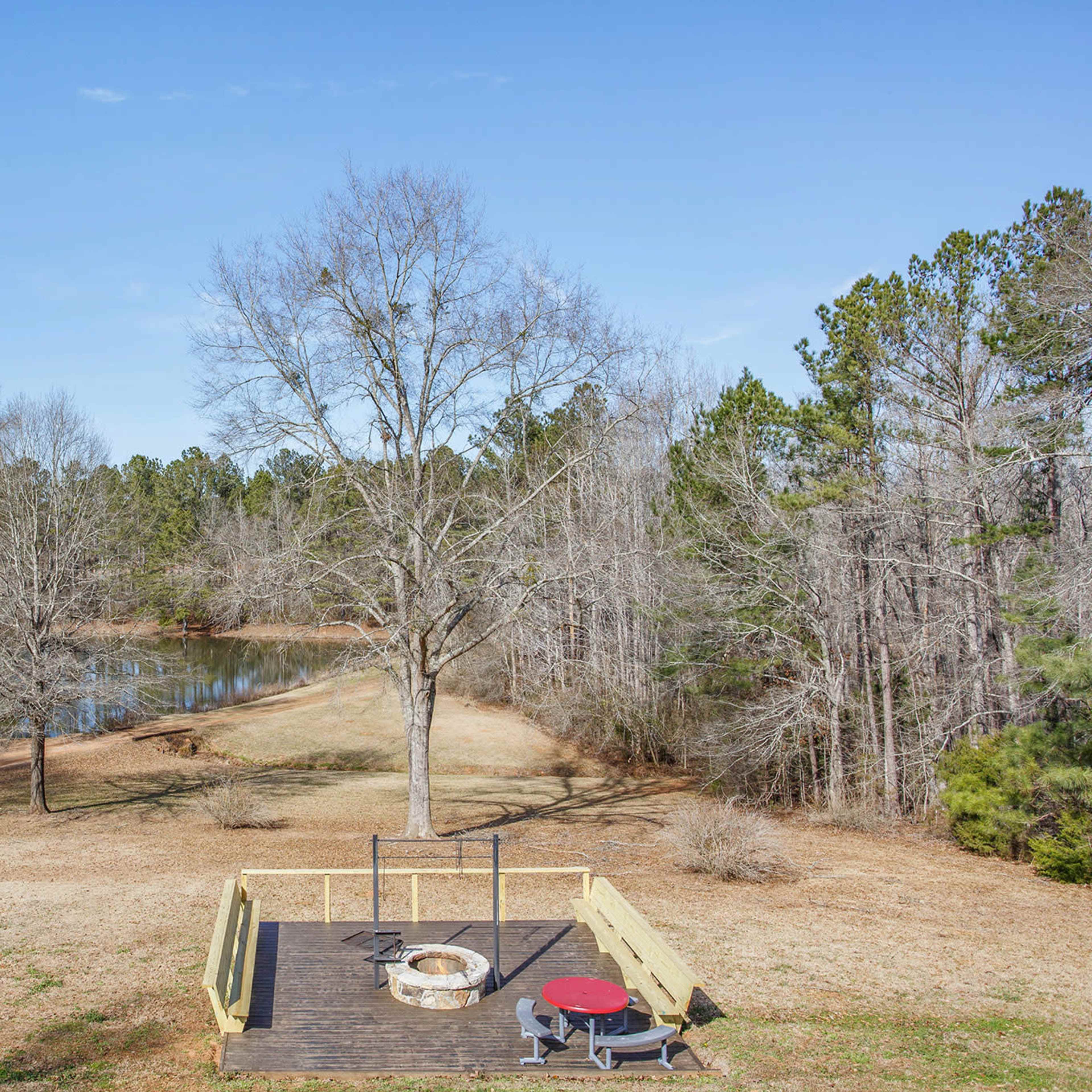 A wooden deck overlooks a calm pond surrounded by trees in a rural landscape.