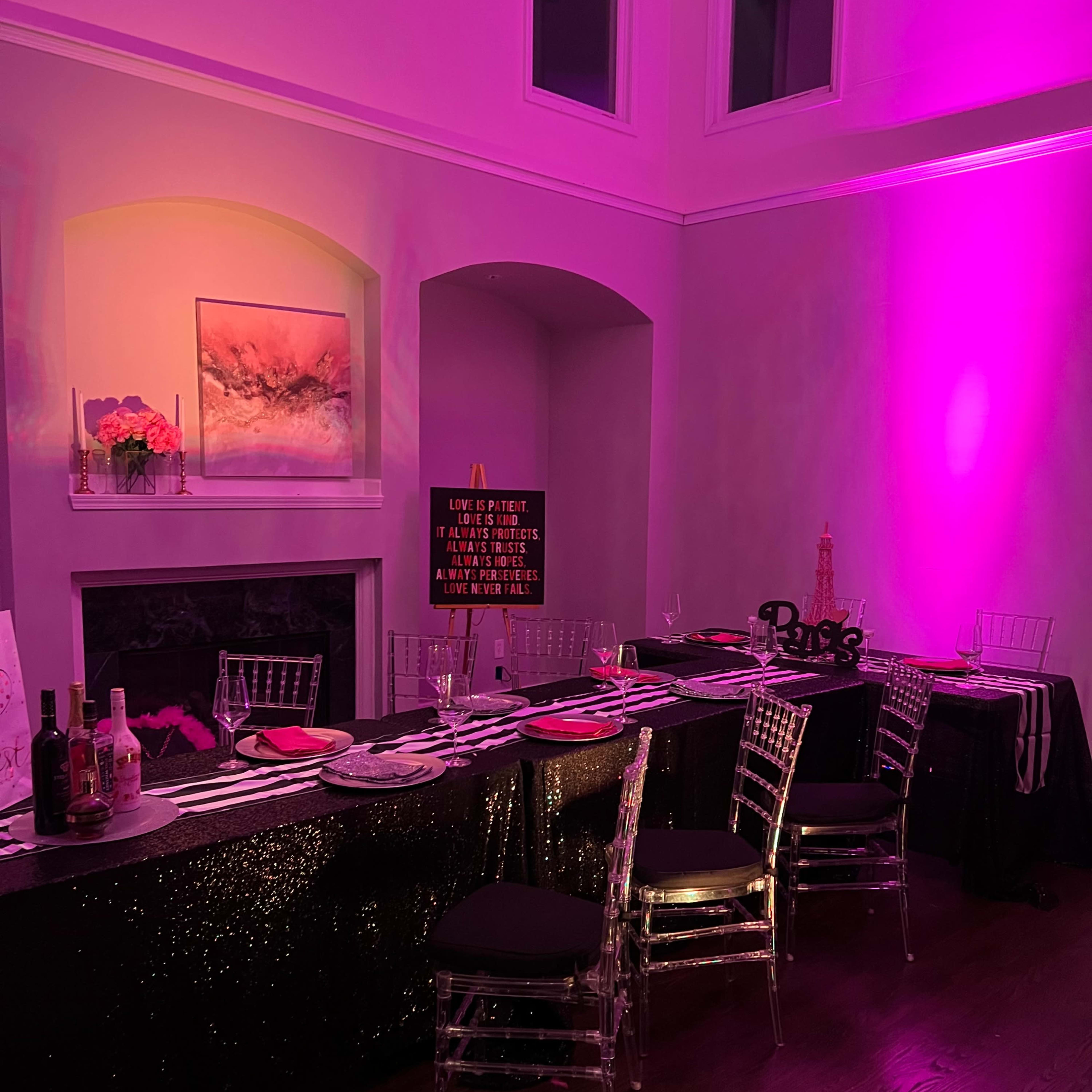 A dining setup with a black and purple color scheme, featuring a long table adorned with decorative items, chairs, and a lit fireplace in the background.