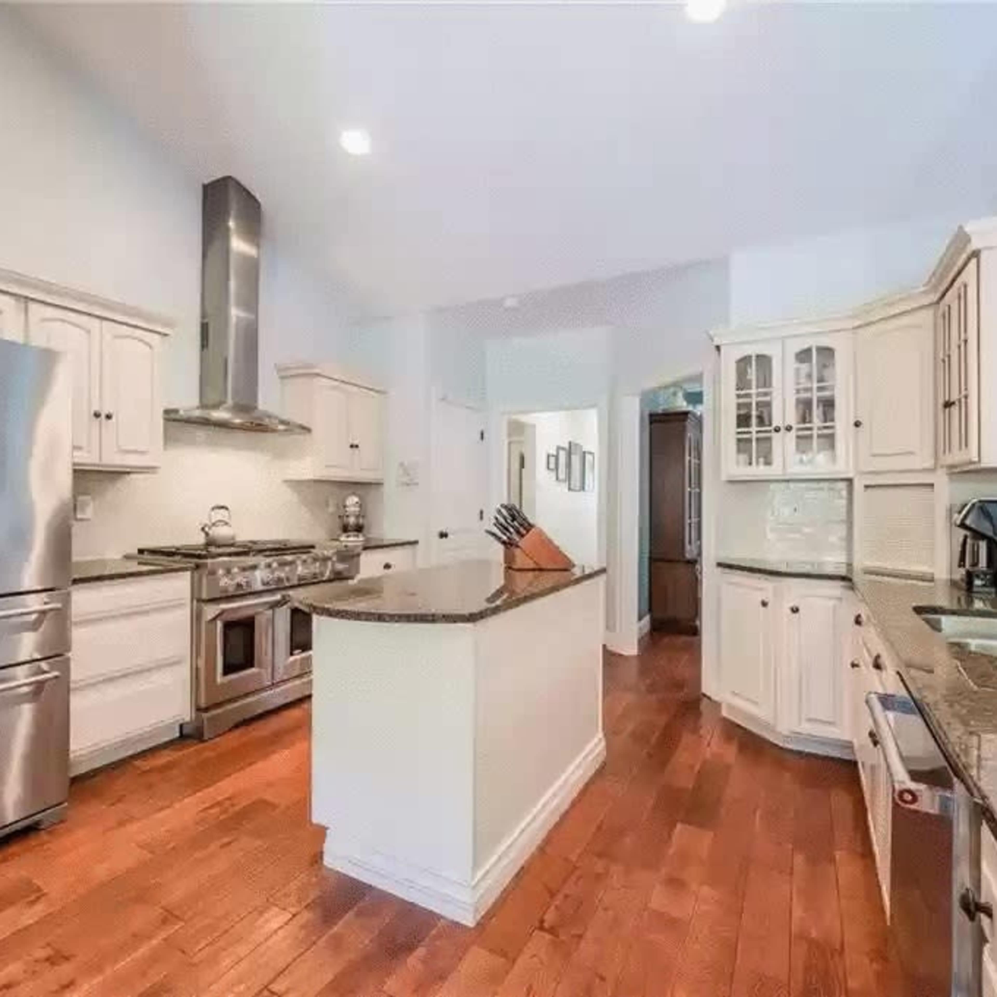 A modern kitchen with stainless steel appliances, wooden flooring, and light-colored cabinetry.