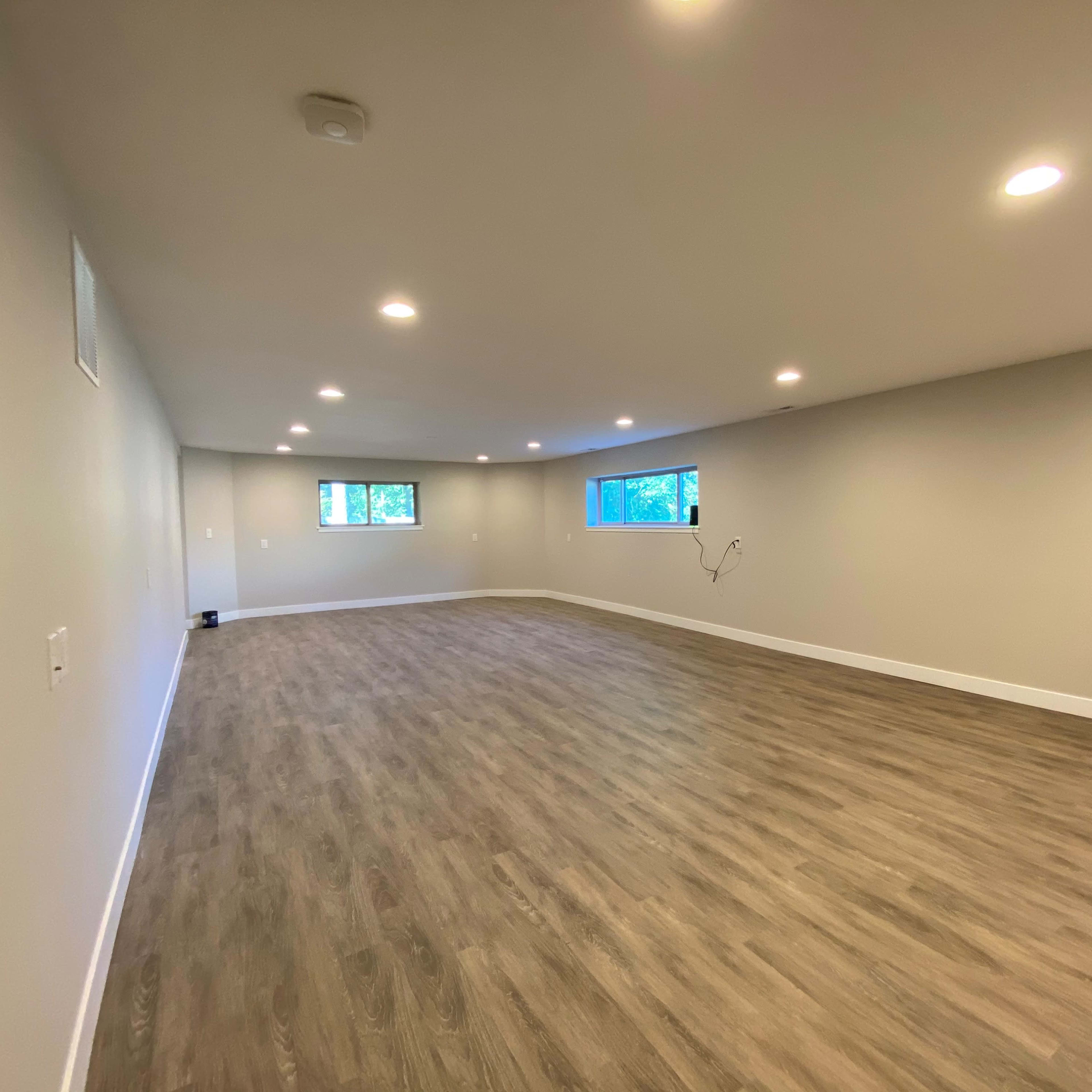 An empty room with wood-like flooring, light walls, and multiple recessed lights illuminating the space.