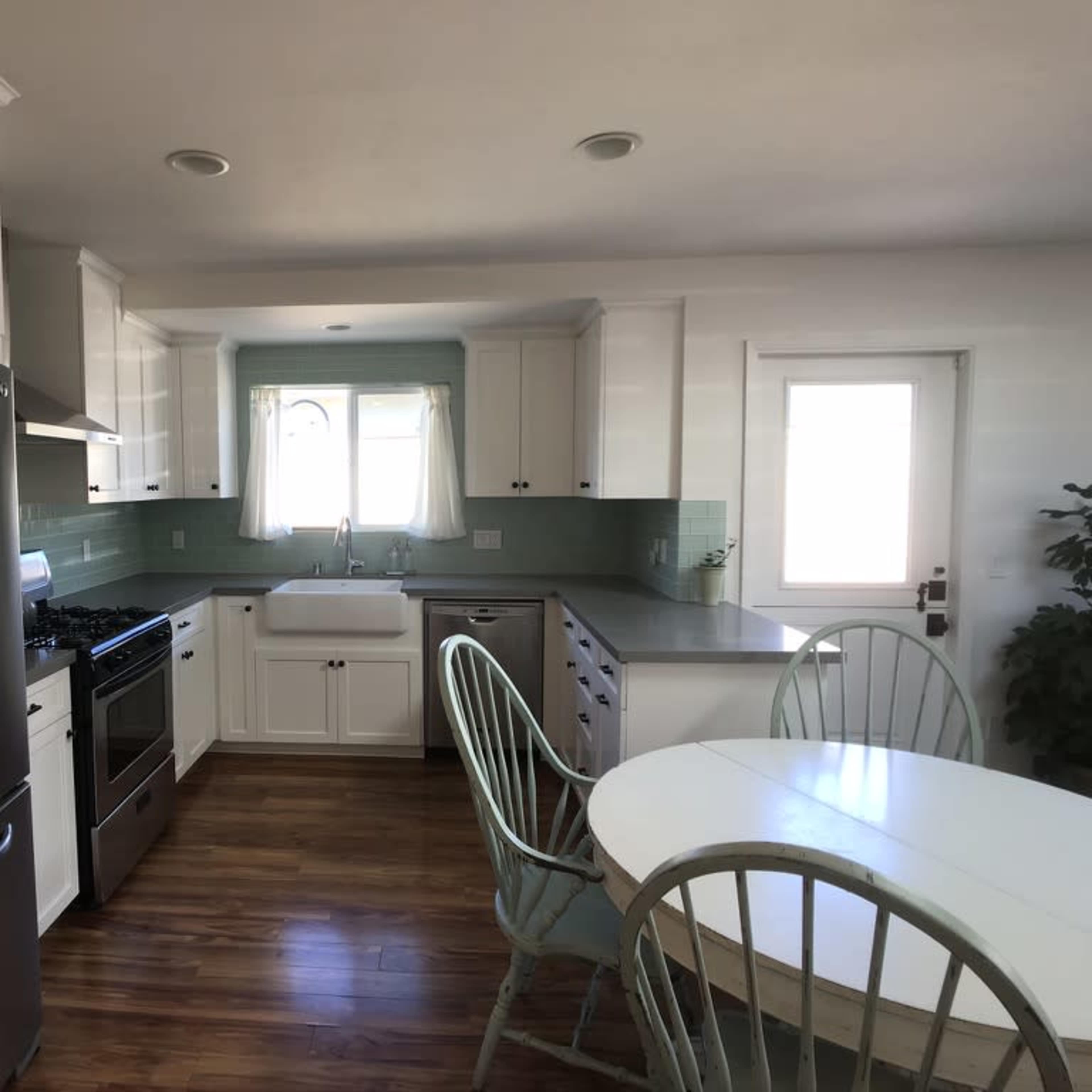 A modern kitchen featuring stainless steel appliances, a large sink, white cabinetry, and a round dining table with green chairs.