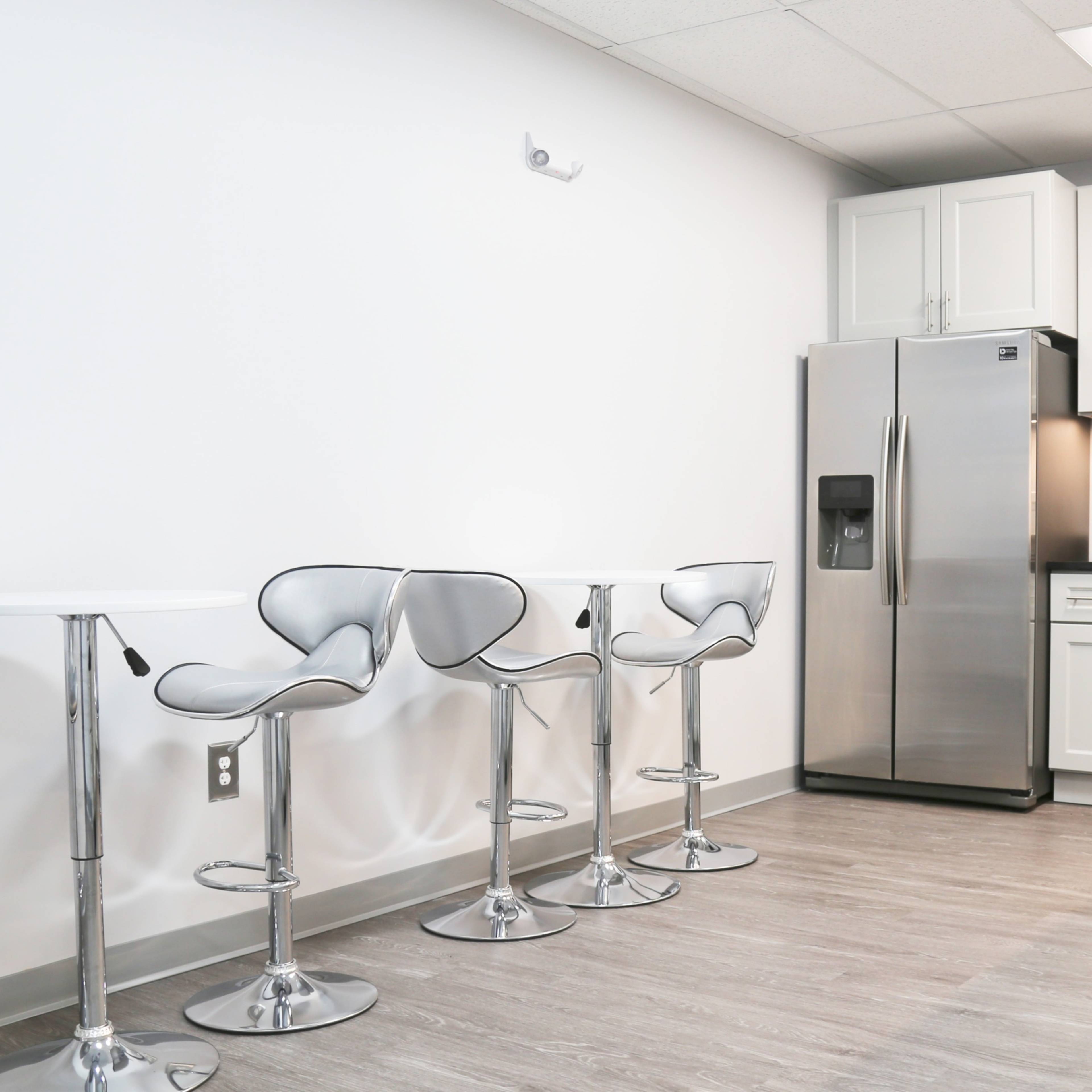 A modern kitchen area featuring stainless steel appliances, white cabinetry, and three high stools at a counter.