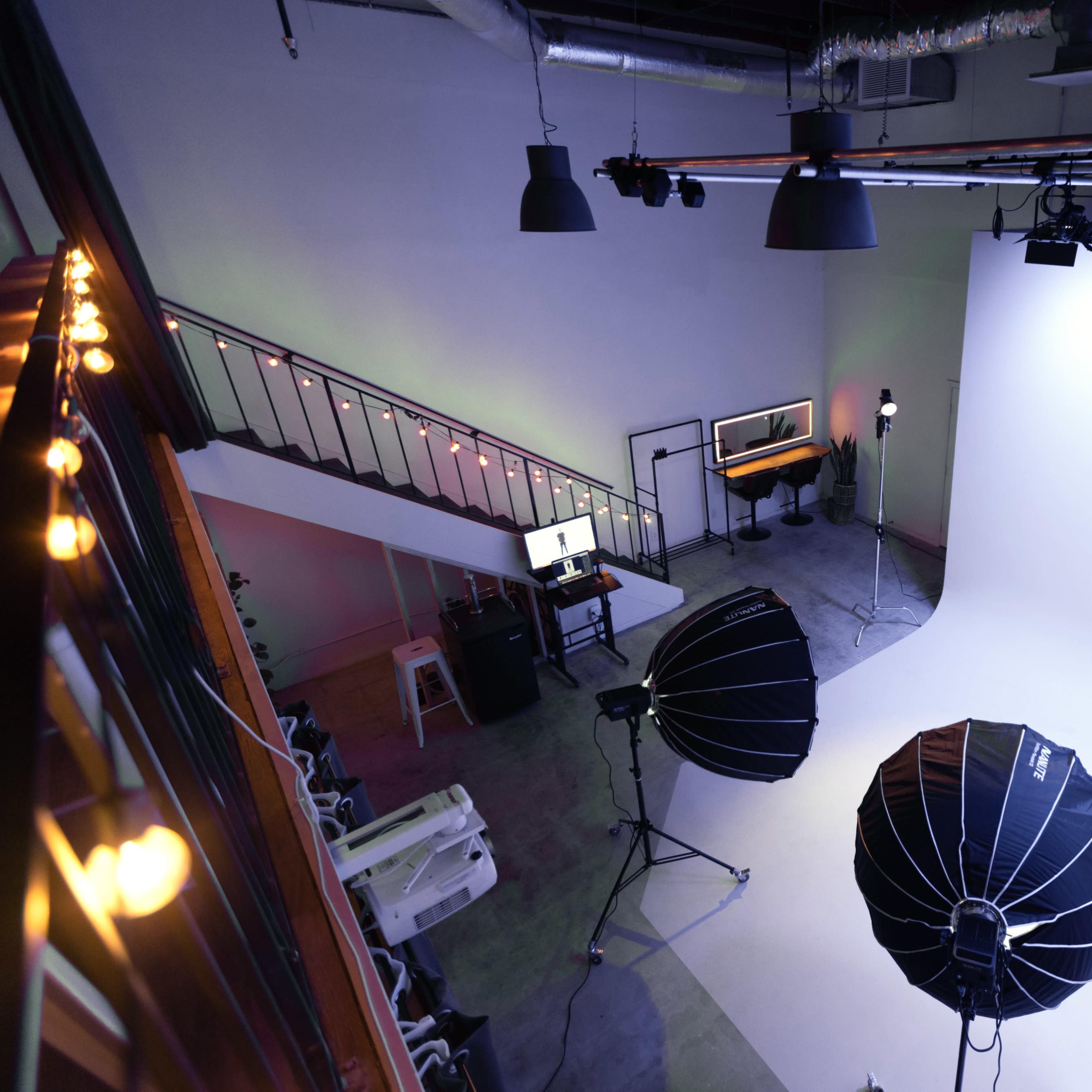 A photography studio with a white backdrop, two large softboxes, and a staircase leading to an upper level.