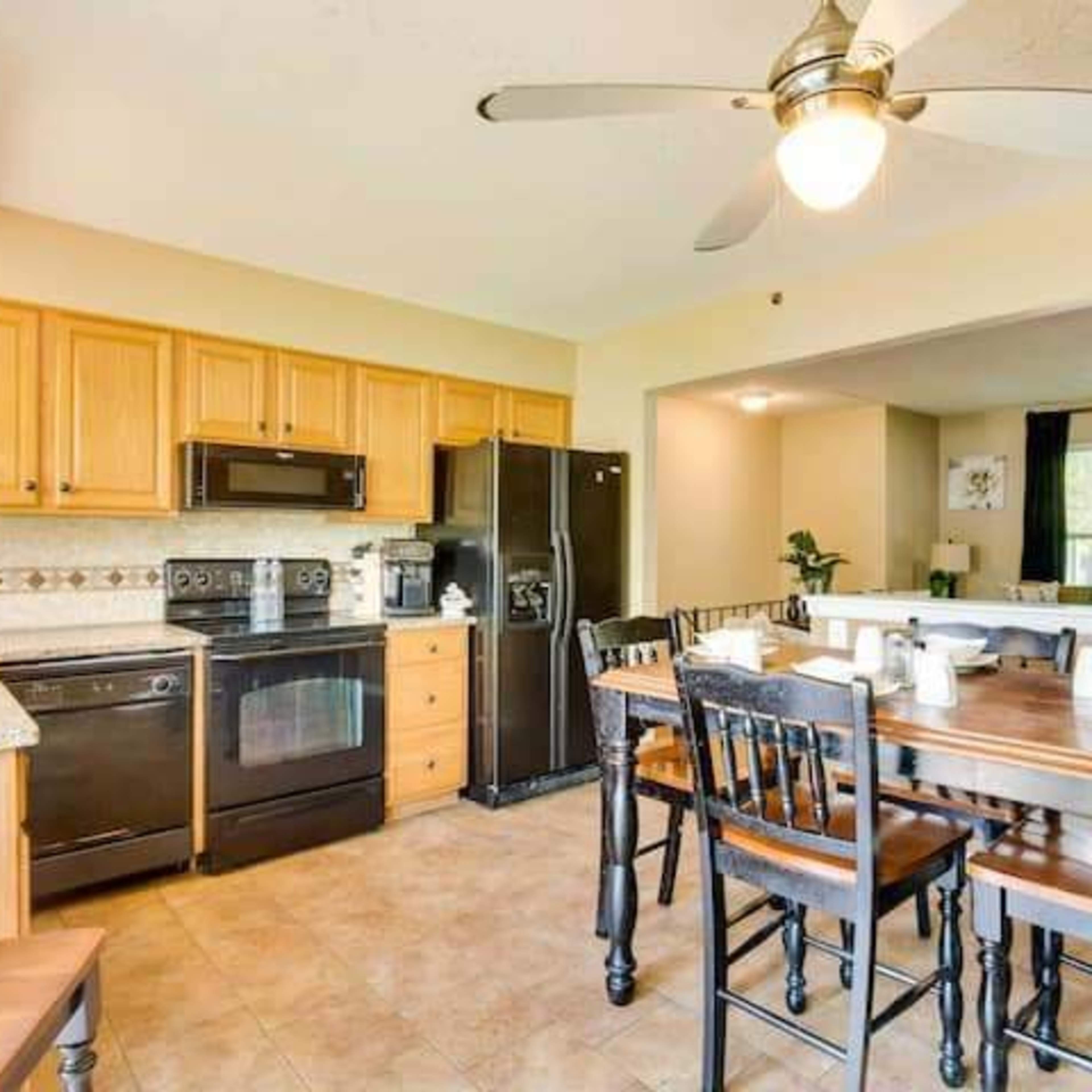A kitchen with wooden cabinets, a dining table set for four, and modern appliances including a stove, microwave, and refrigerator.