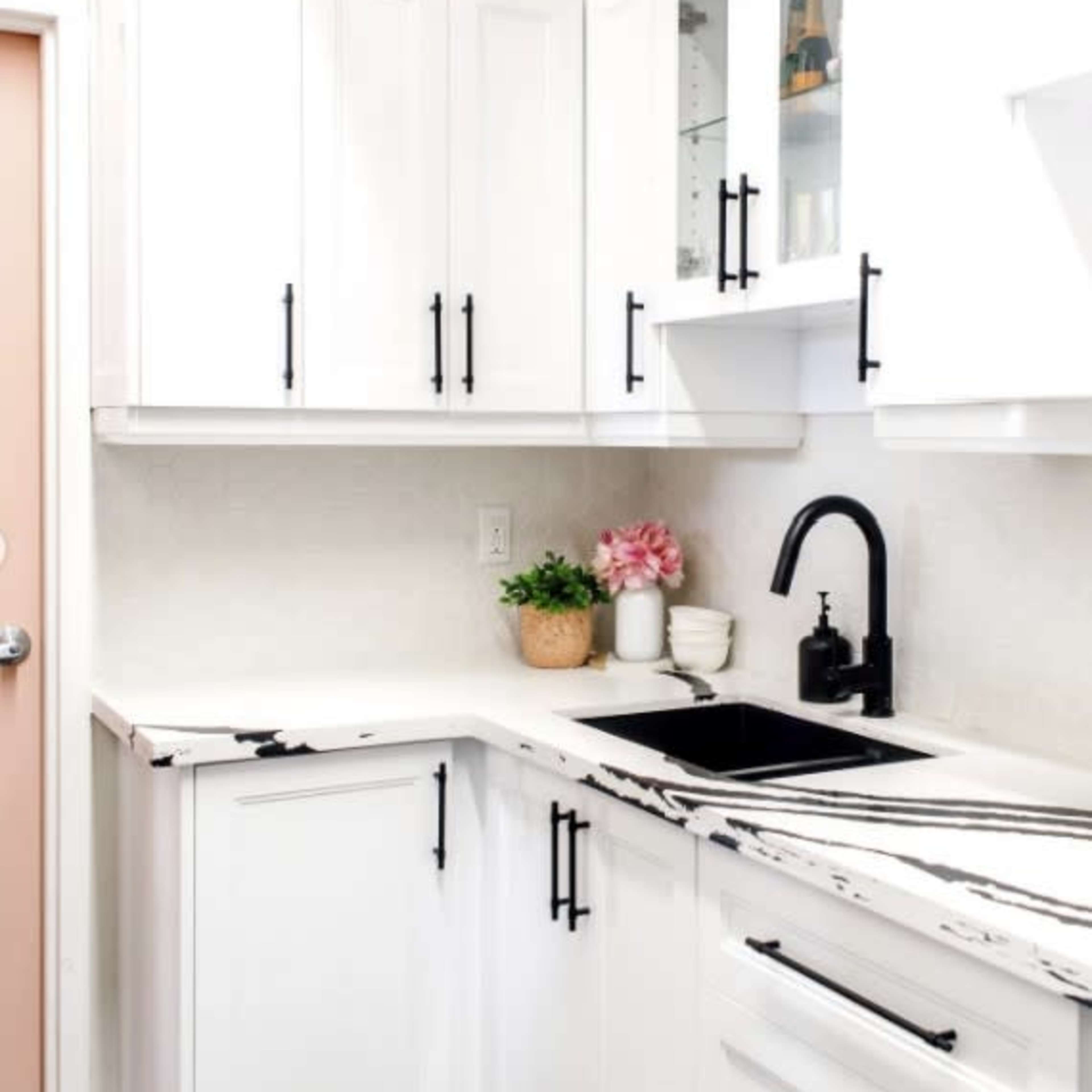 A modern kitchen with white cabinets, a black faucet, and a countertop featuring black and white marble patterns.