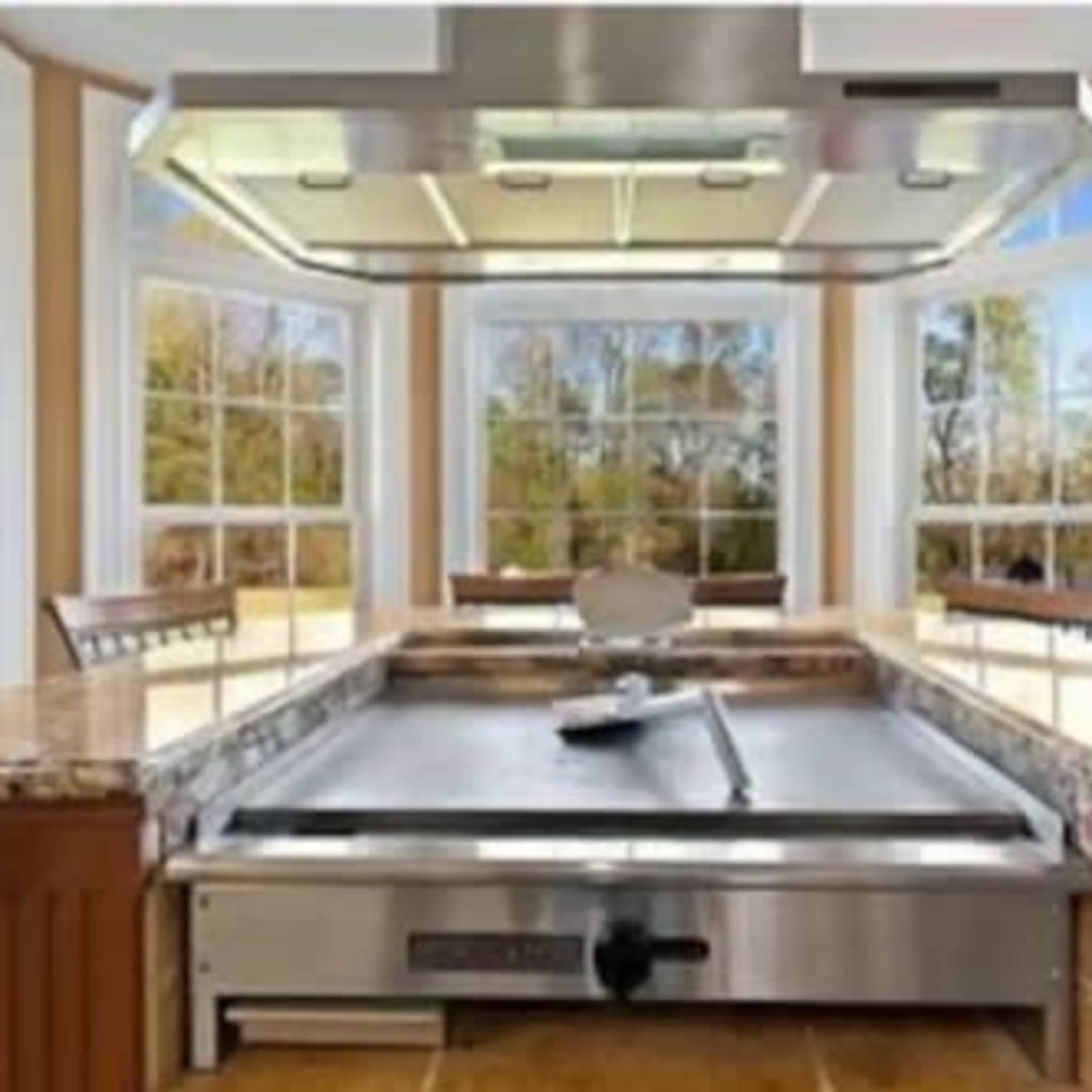 A spacious kitchen with a large griddle surface at the center, surrounded by tall windows that let in natural light.