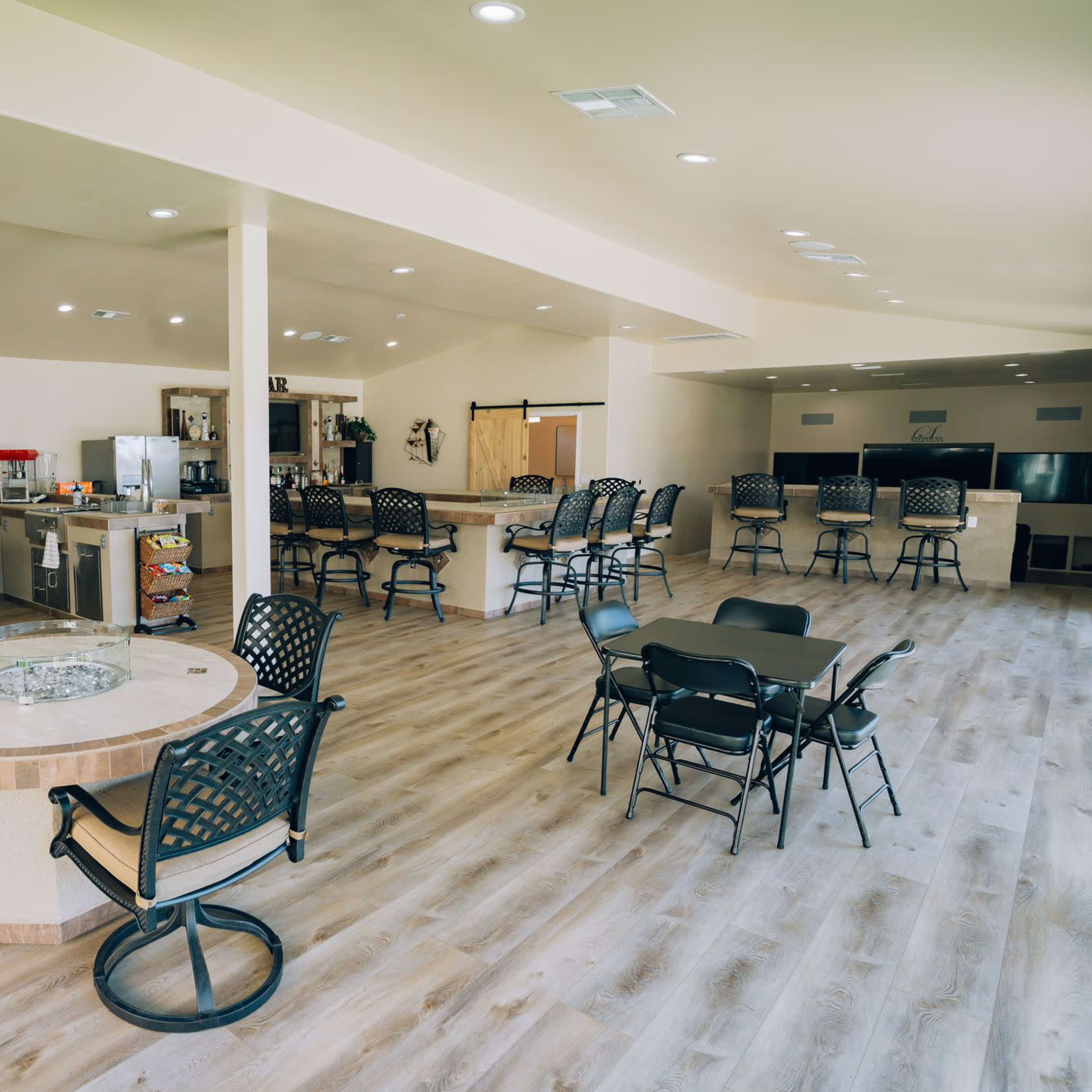 A spacious indoor dining area featuring a bar with high chairs, several dining tables, and a kitchen area equipped with countertops and appliances.
