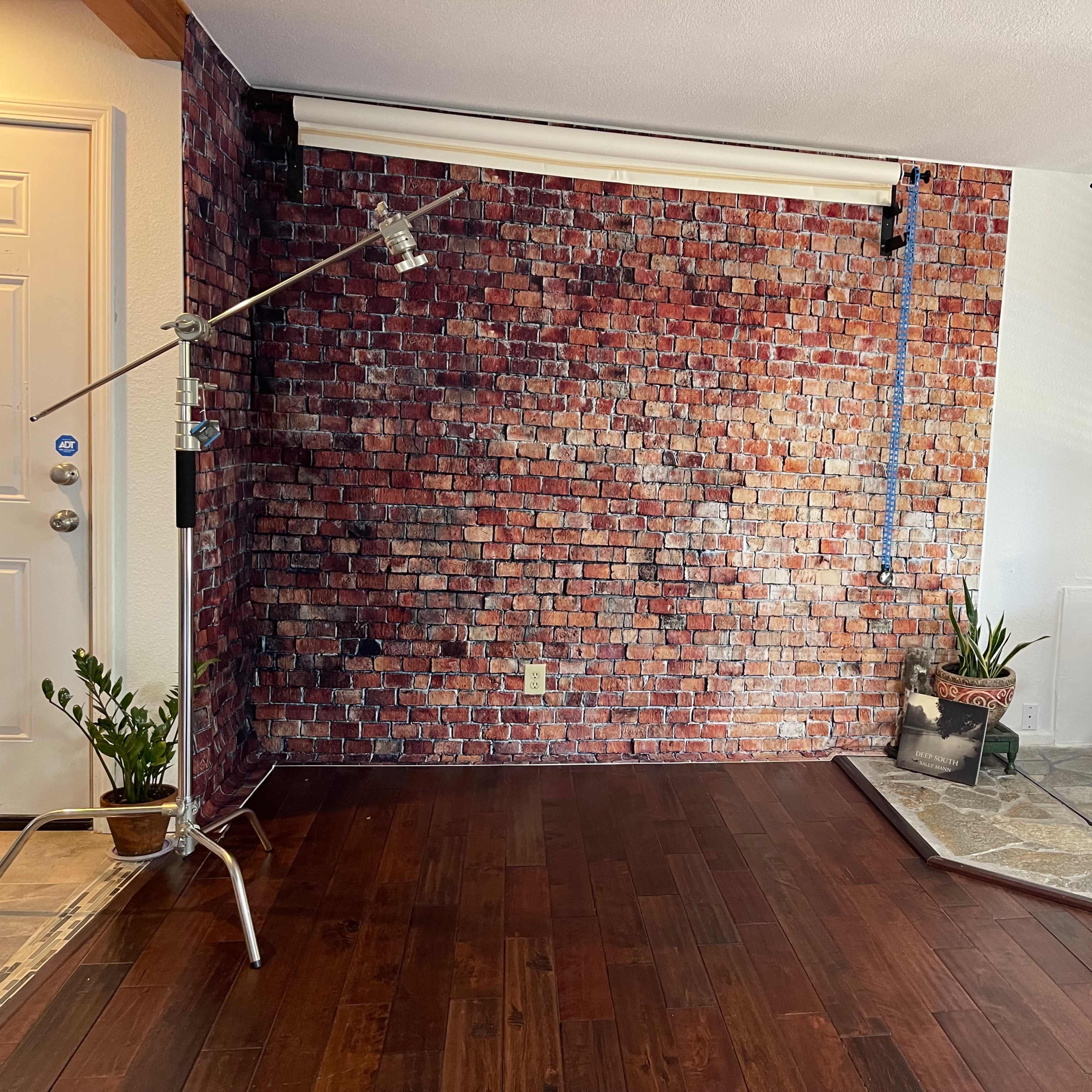 A studio space with a brick-patterned backdrop, two lighting stands, a wood stove, and a stone flooring section.