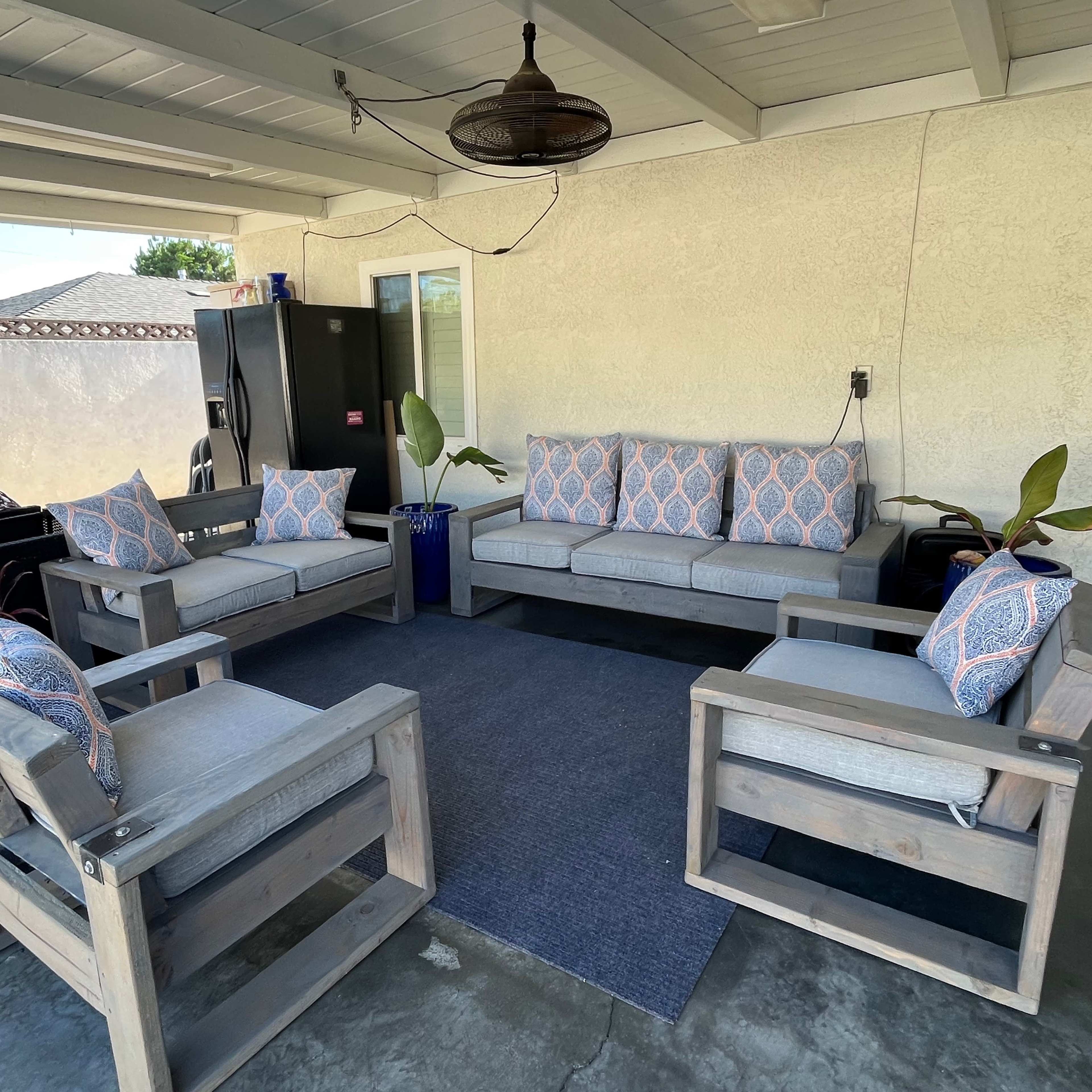 A patio with a set of gray outdoor sofas and chairs arranged around a blue rug under a covered area.