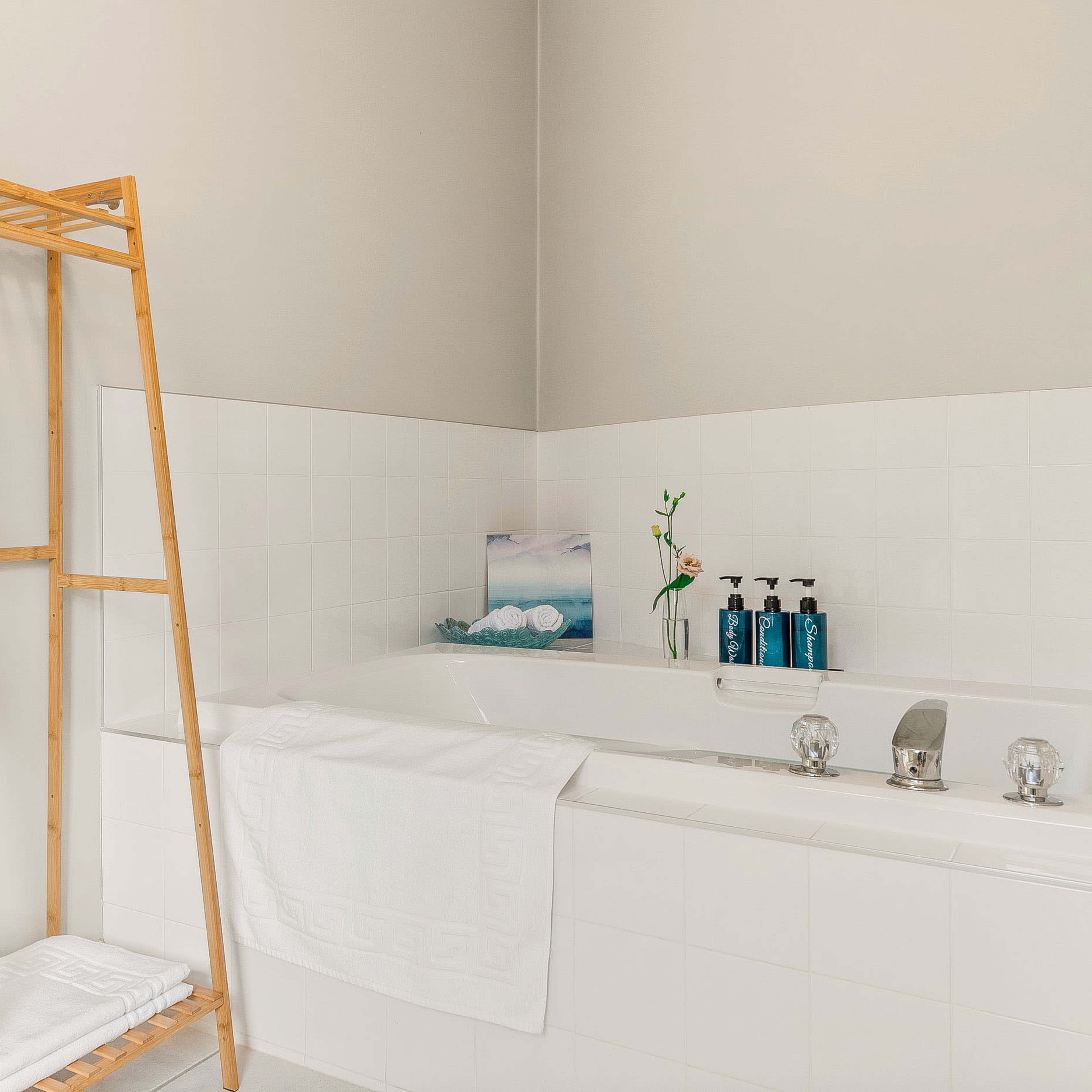 A wooden towel rack holds neatly rolled towels next to a white bathtub with bottles of toiletries displayed on the edge.