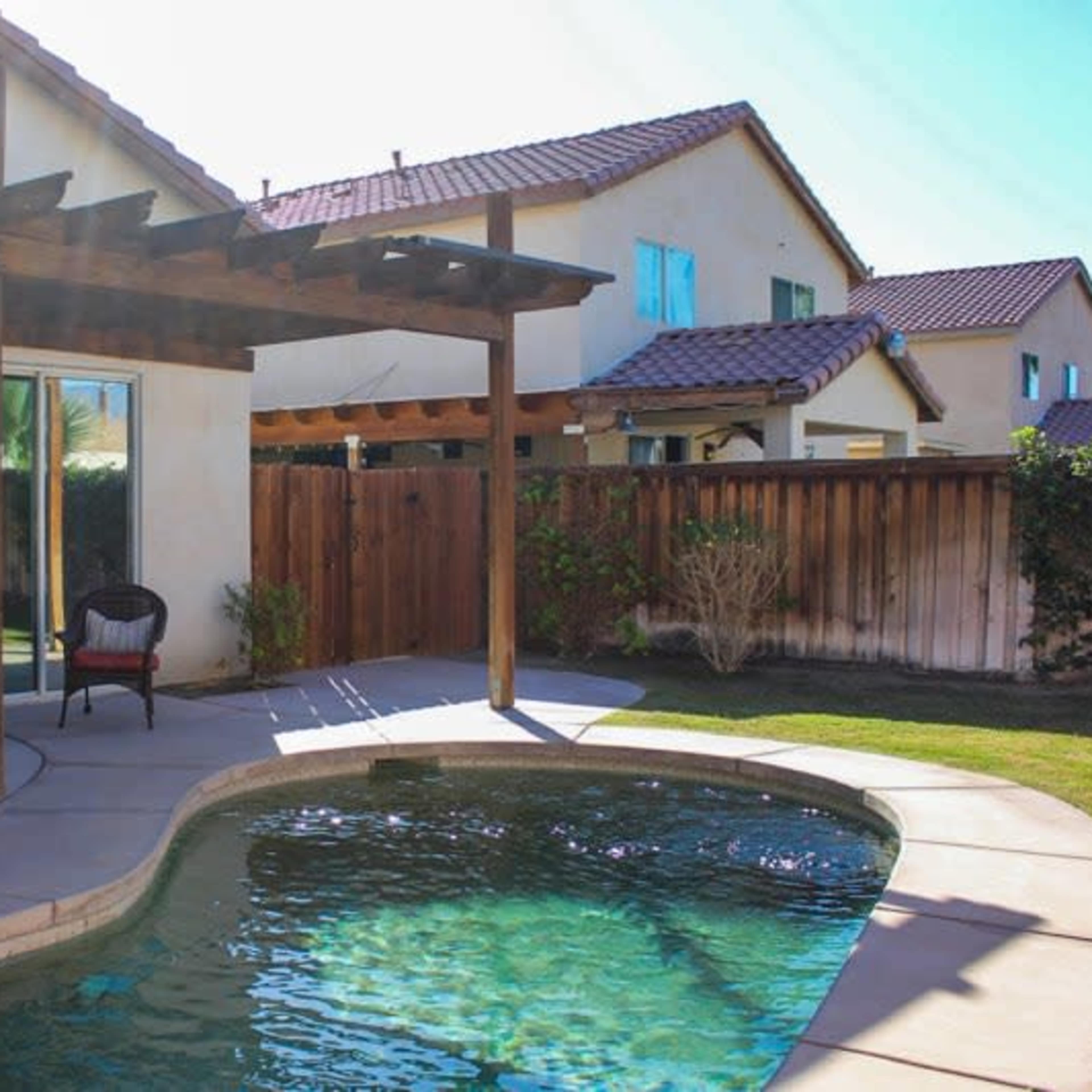 A backyard with a swimming pool, a wooden pergola, and outdoor seating beside a house.