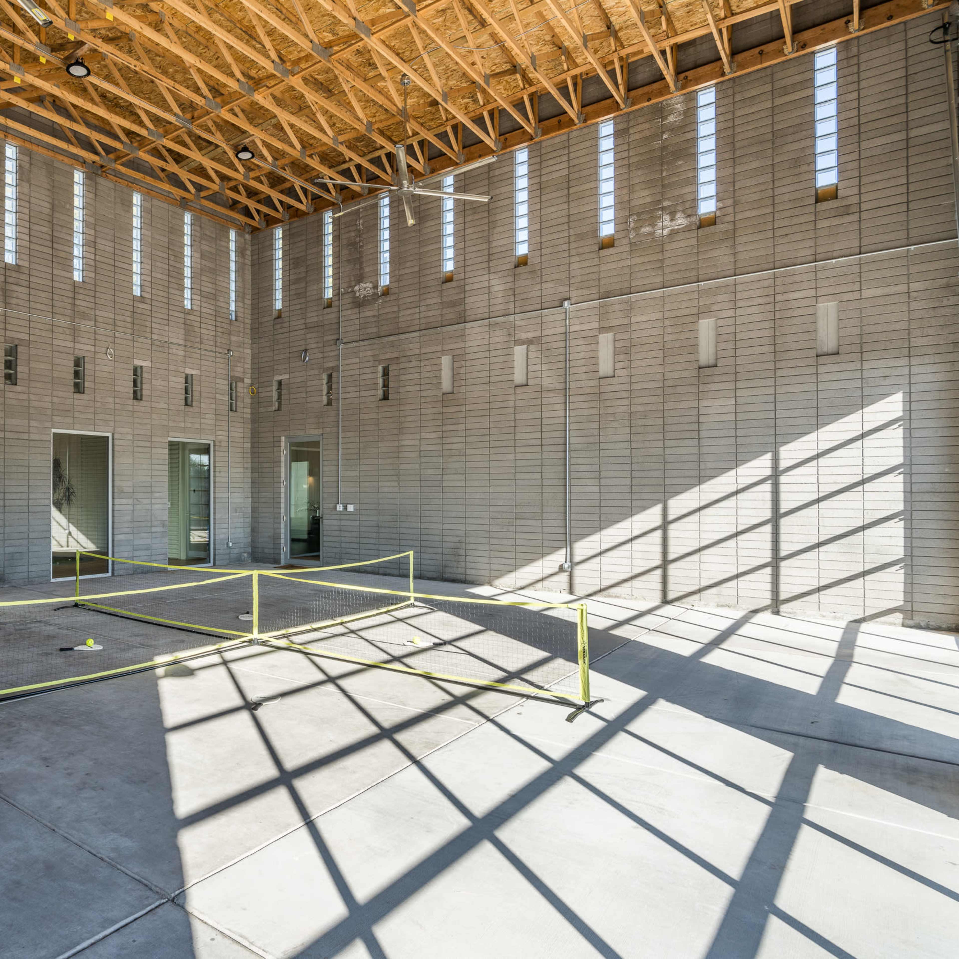 An empty interior space with concrete block walls, large windows allowing light to stream in, and a yellow safety barrier in the center of the floor.