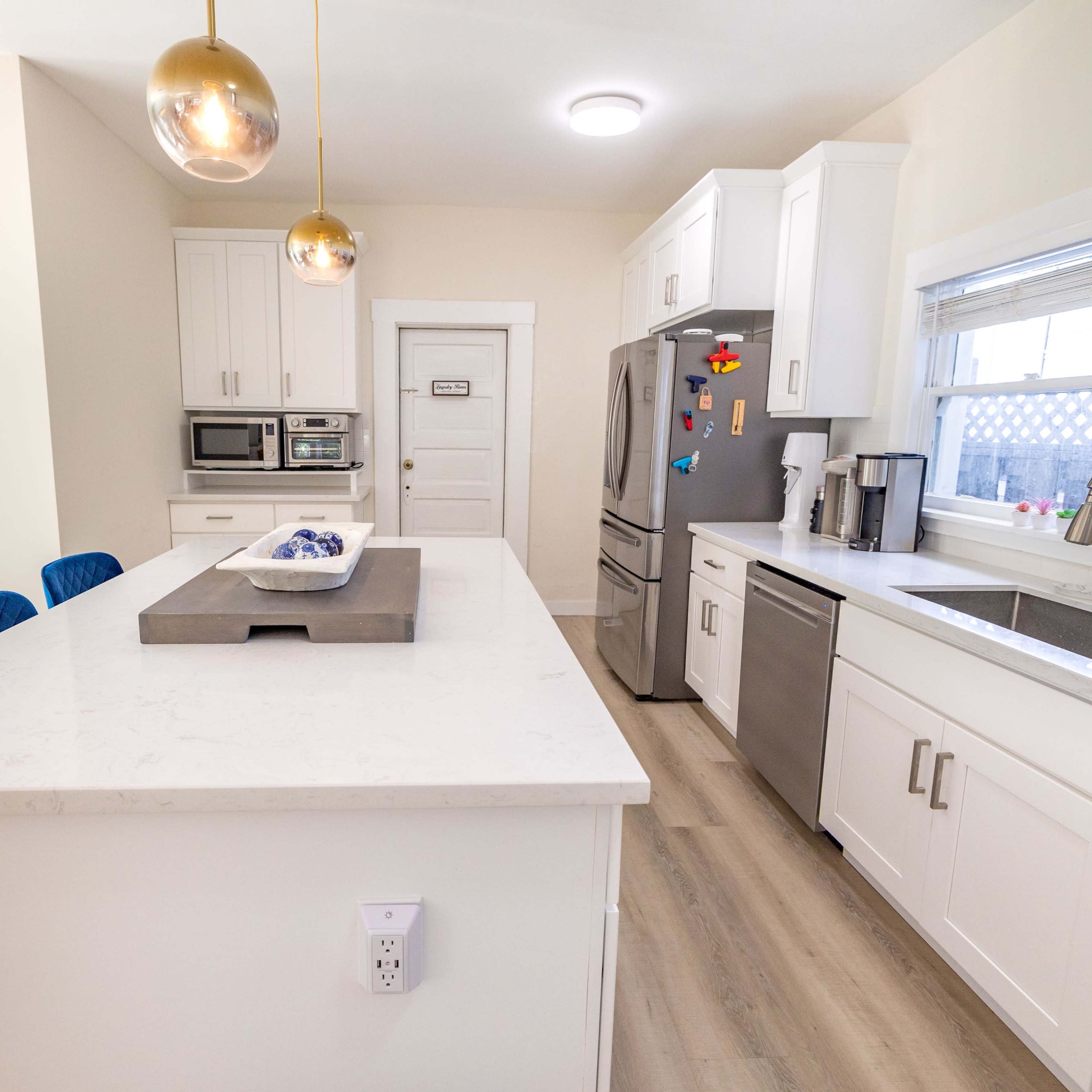 The kitchen features white cabinetry, stainless steel appliances, and a central island with blue bar stools and pendant lighting.