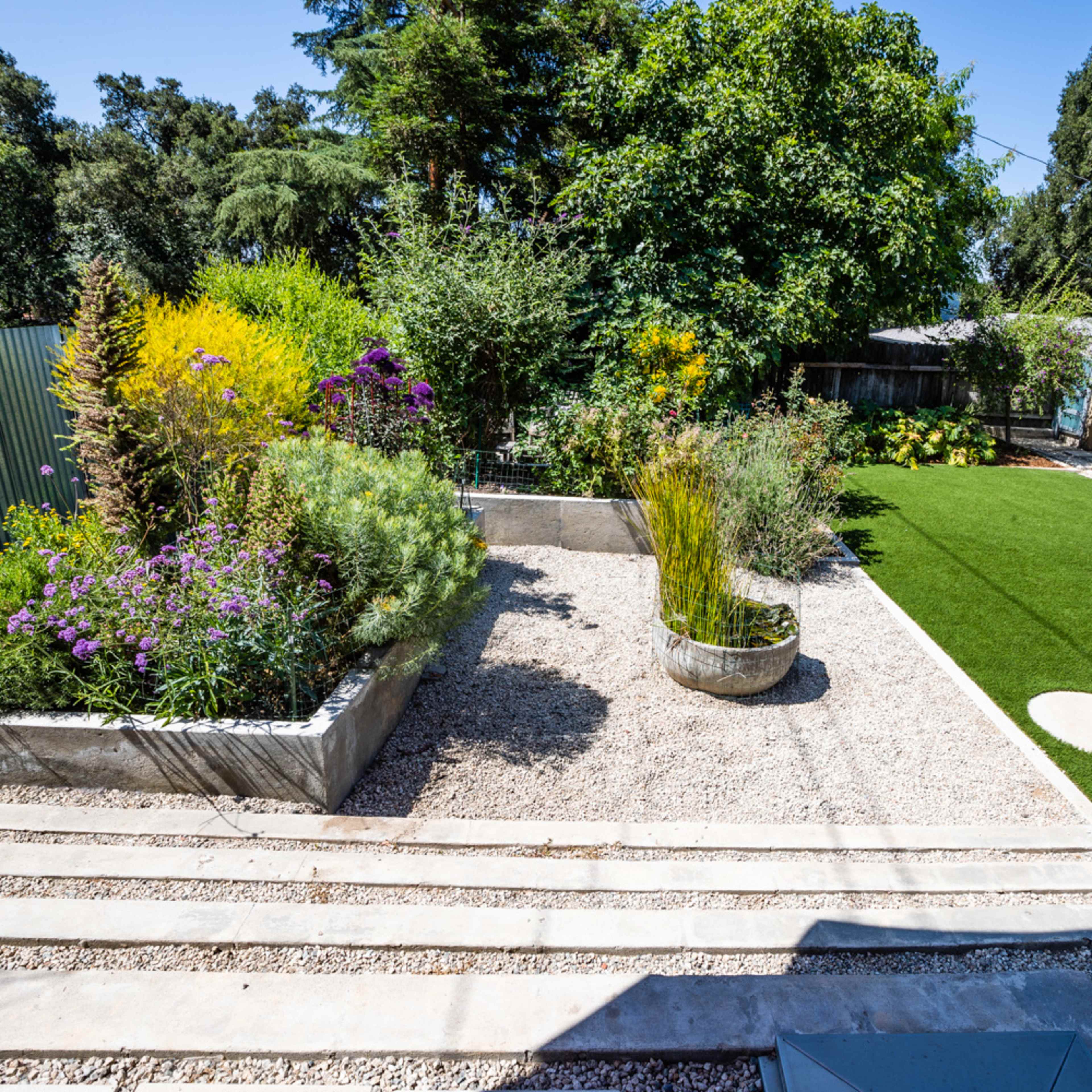 A landscaped garden featuring a gravel area, planters with vibrant plants, and a section of artificial turf alongside a modern home.