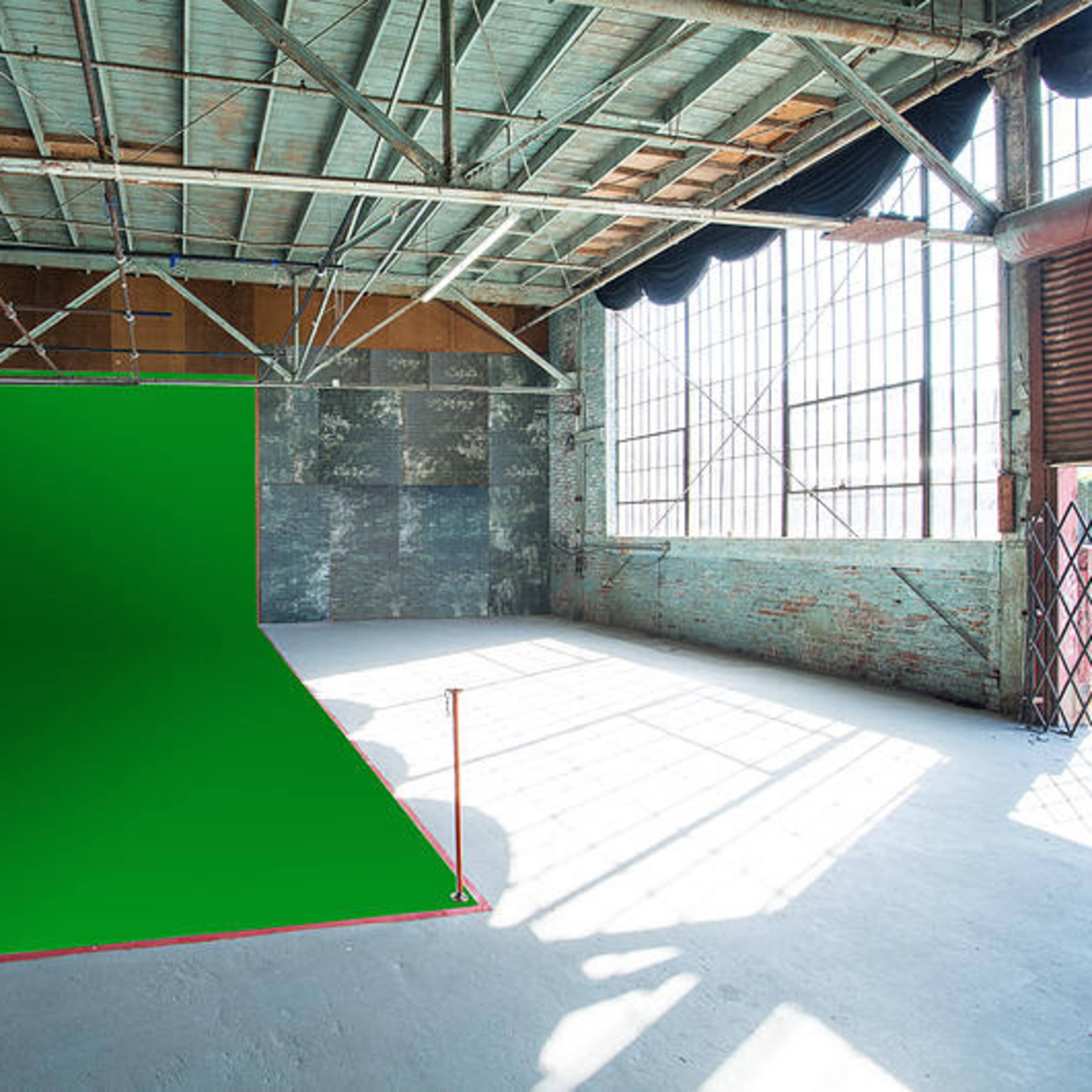 A spacious studio with a green backdrop, large windows, and exposed beams.
