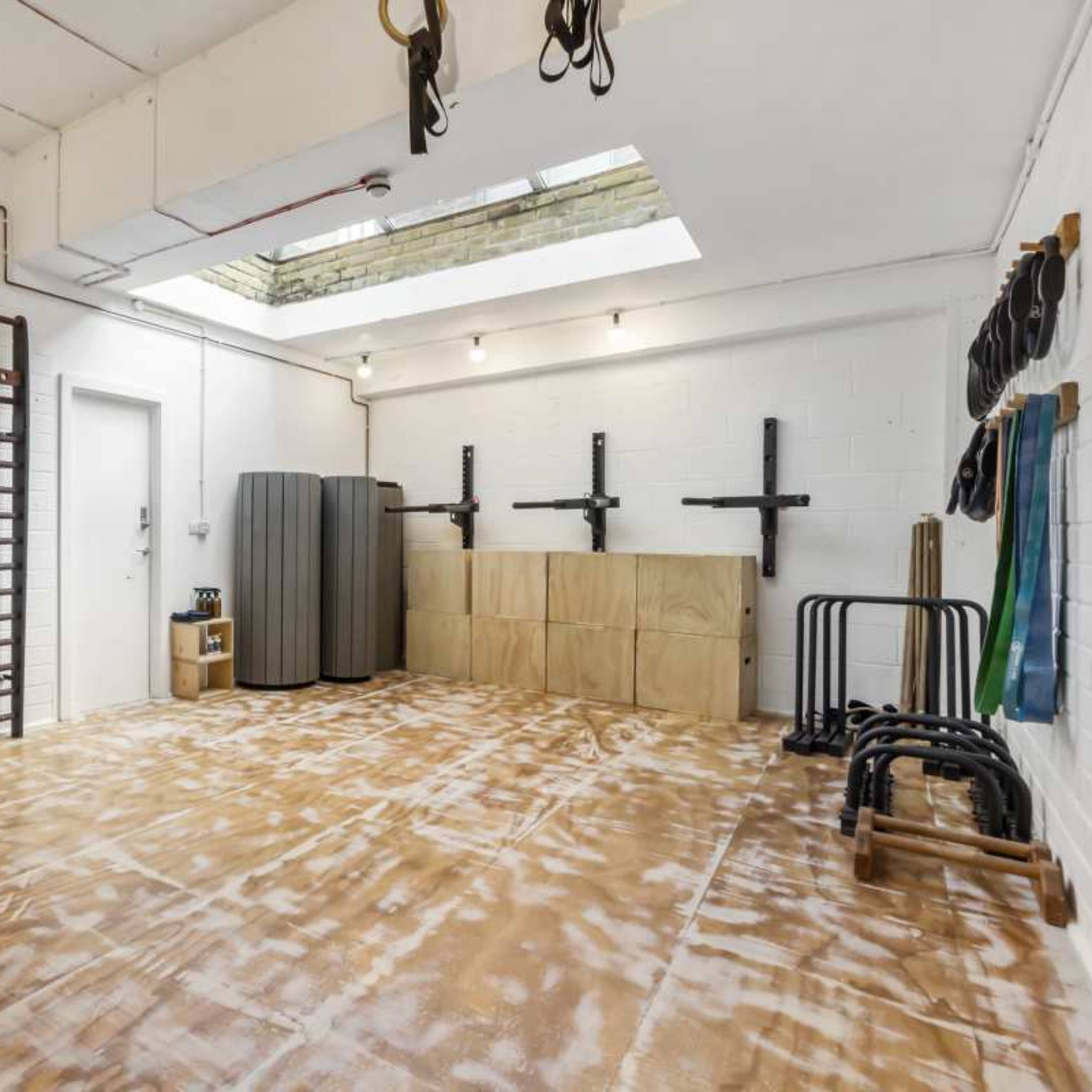 A spacious, empty gym or workout room with wooden wall bars, a large gray storage cabinet, and various fitness equipment neatly arranged against the walls.