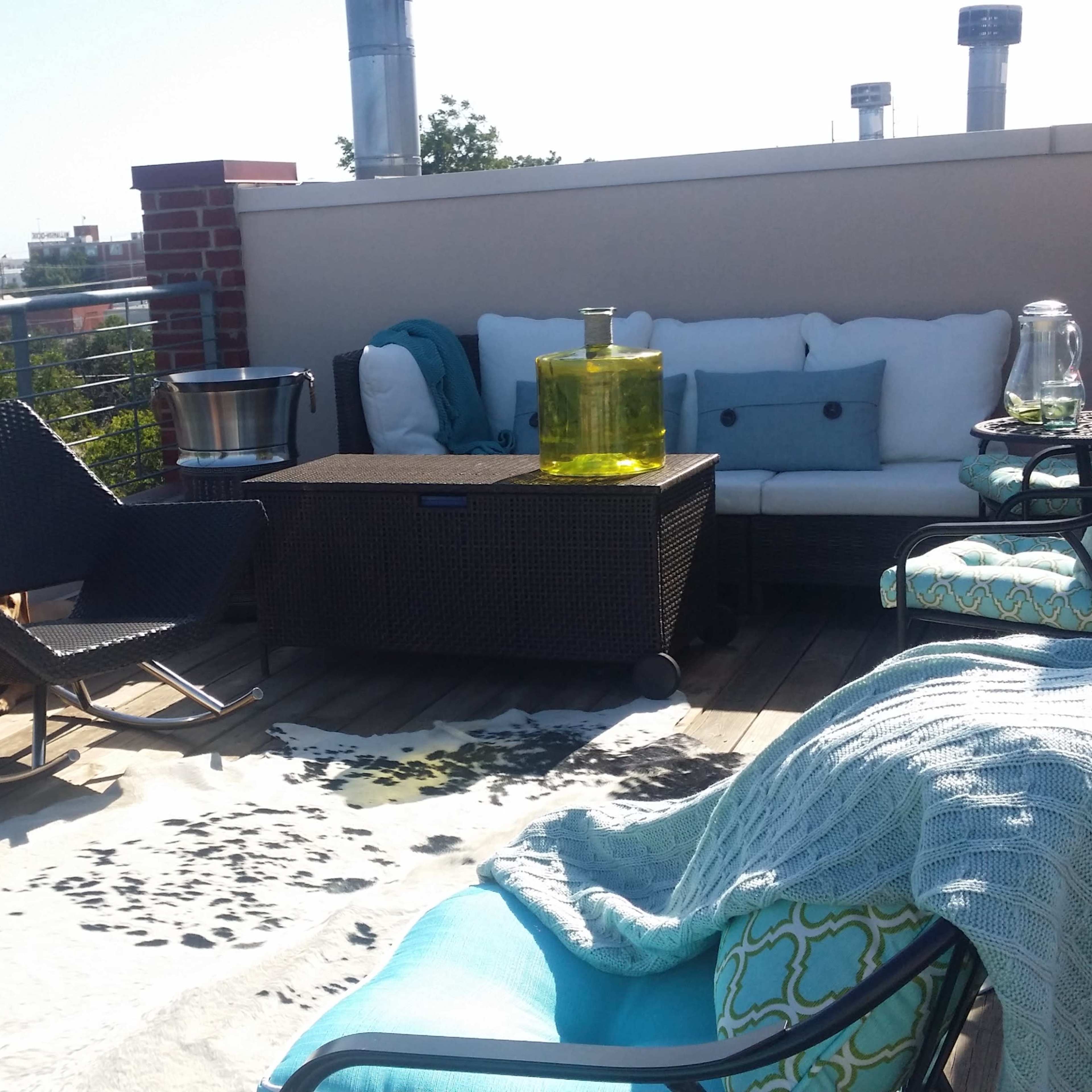 The rooftop terrace features a sectional sofa, a glass coffee table, and a few lounge chairs arranged around a decorative cowhide rug.