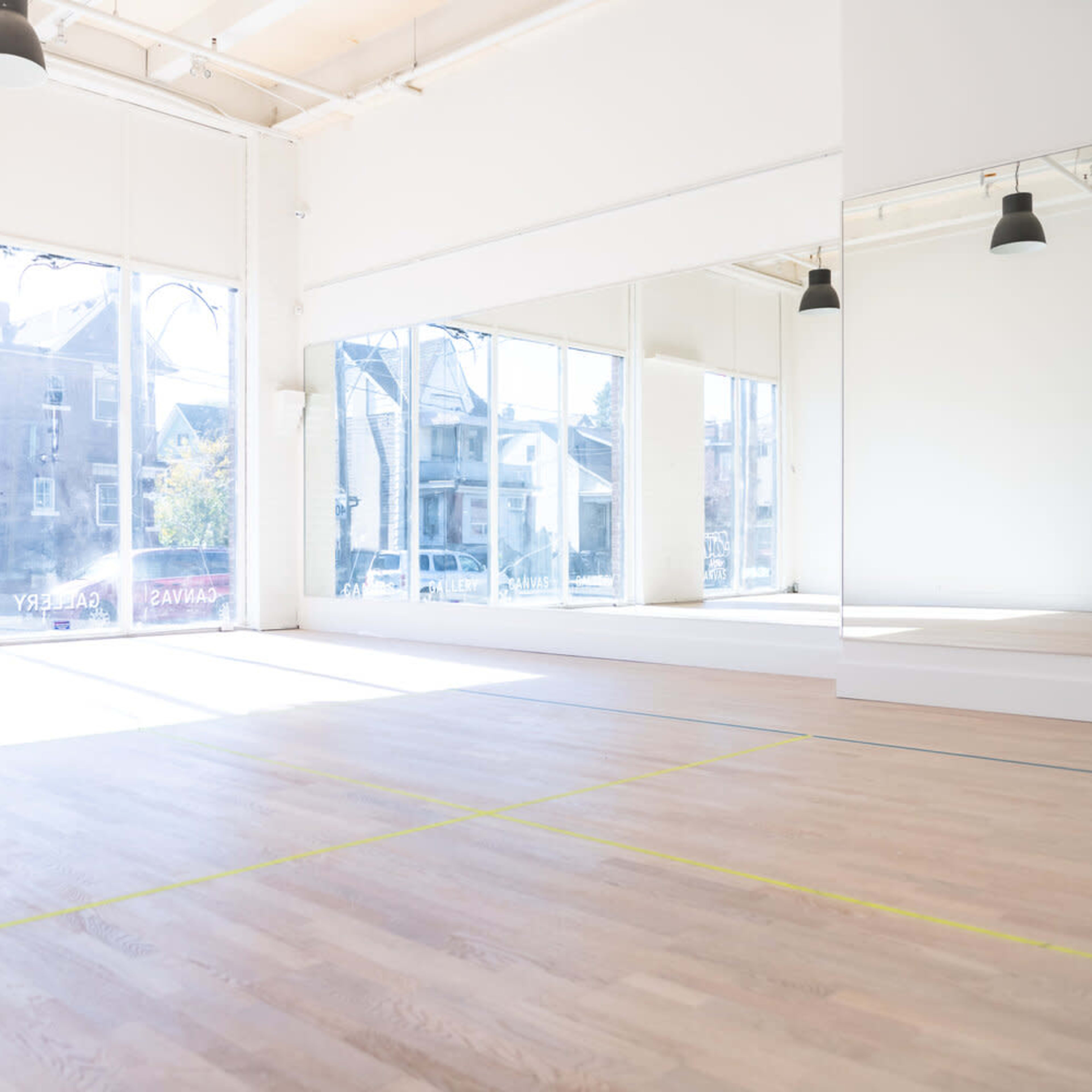A spacious, well-lit empty studio with large windows and a mirrored wall.