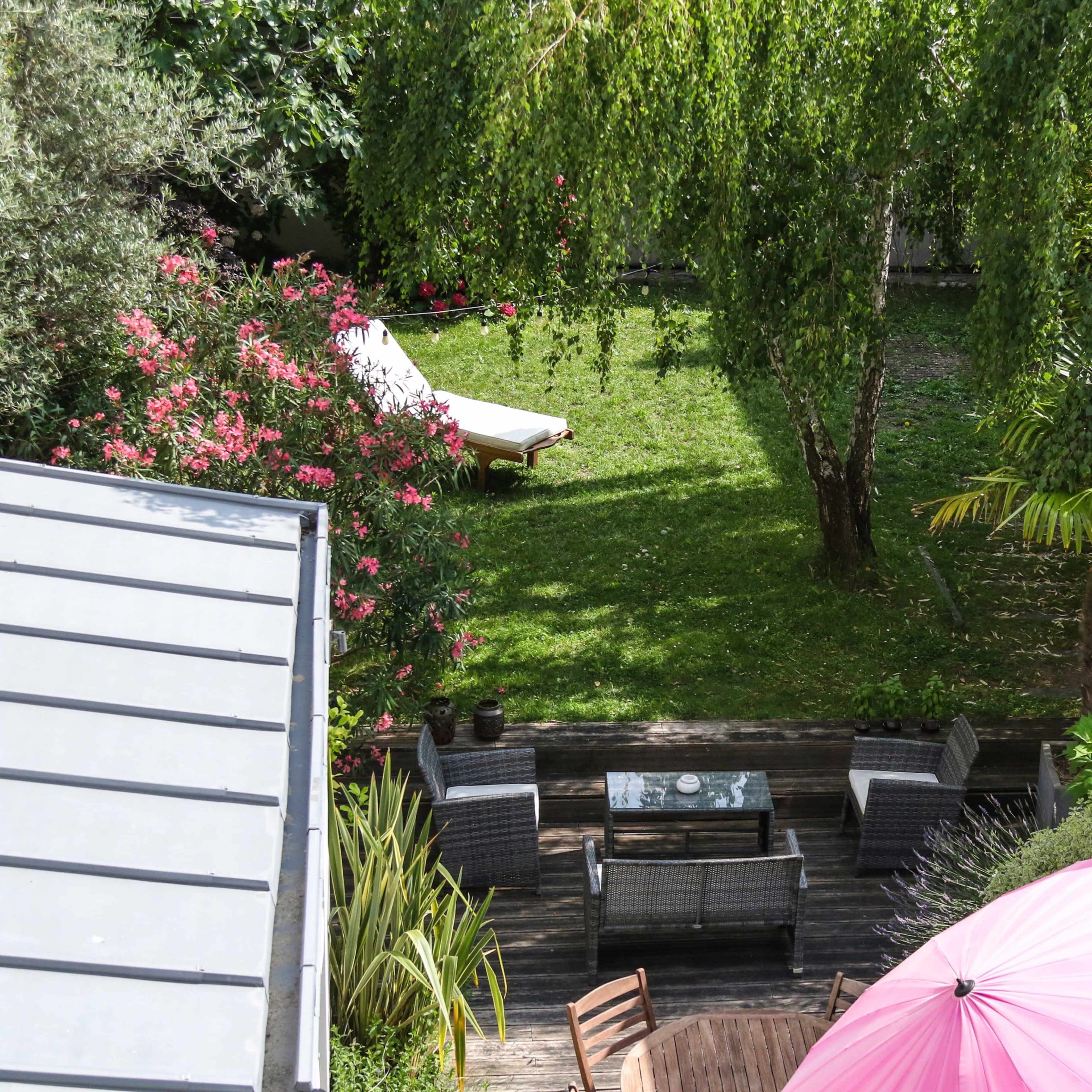 A landscaped backyard featuring green grass, patio furniture, and a large pink umbrella.