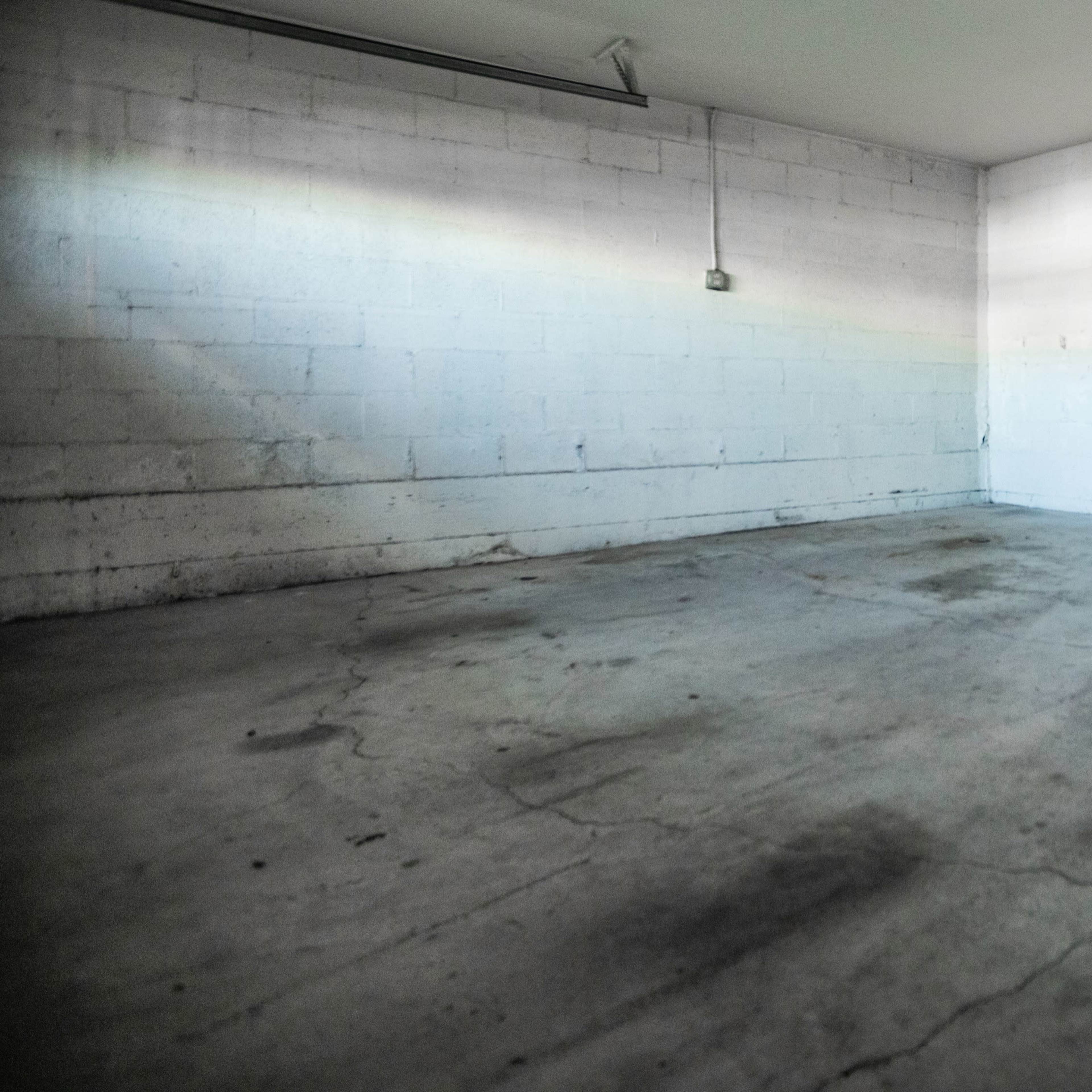 An empty room with cracked concrete flooring and bare white walls illuminated by overhead light.