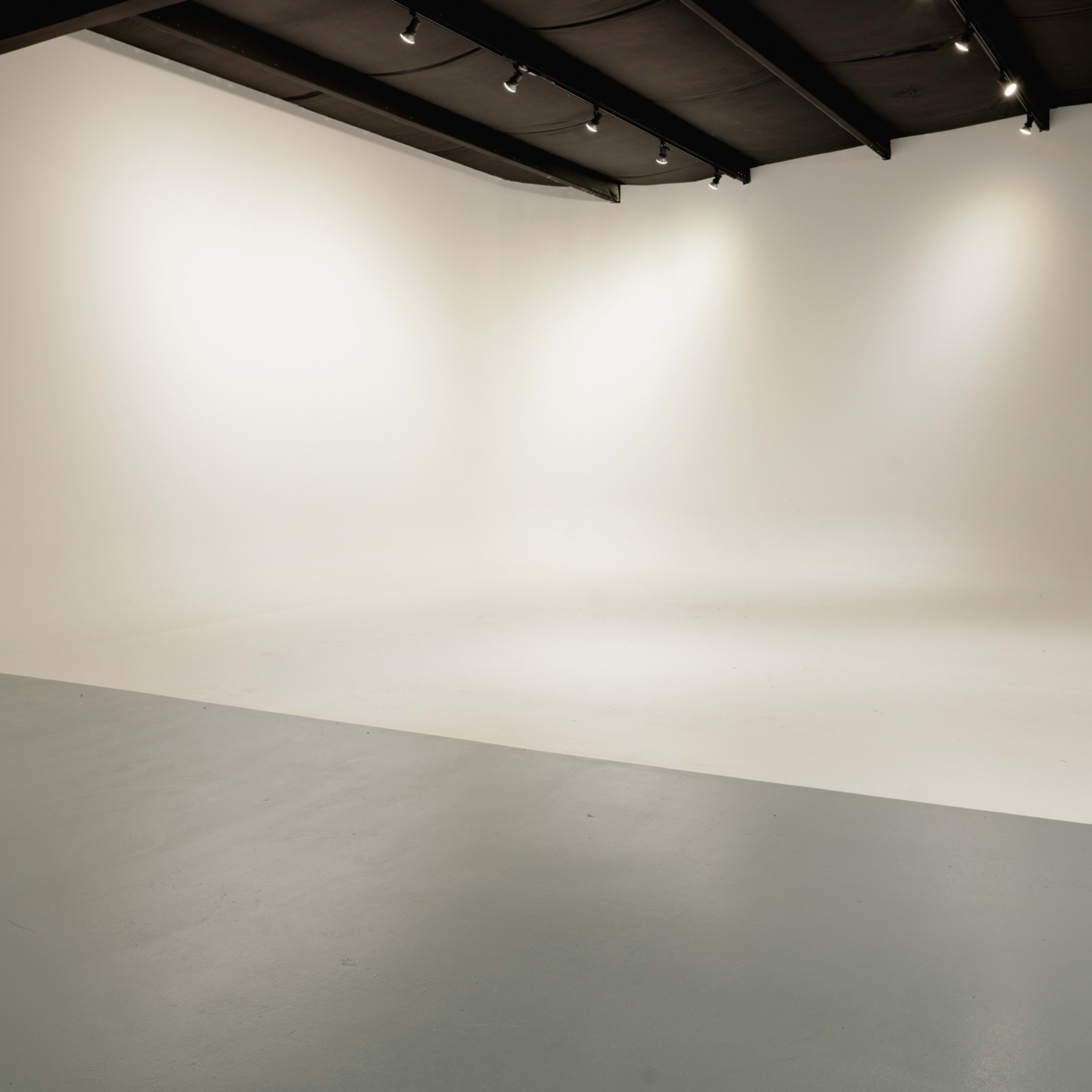 A spacious photography studio with a seamless white background and smooth, light-colored flooring.