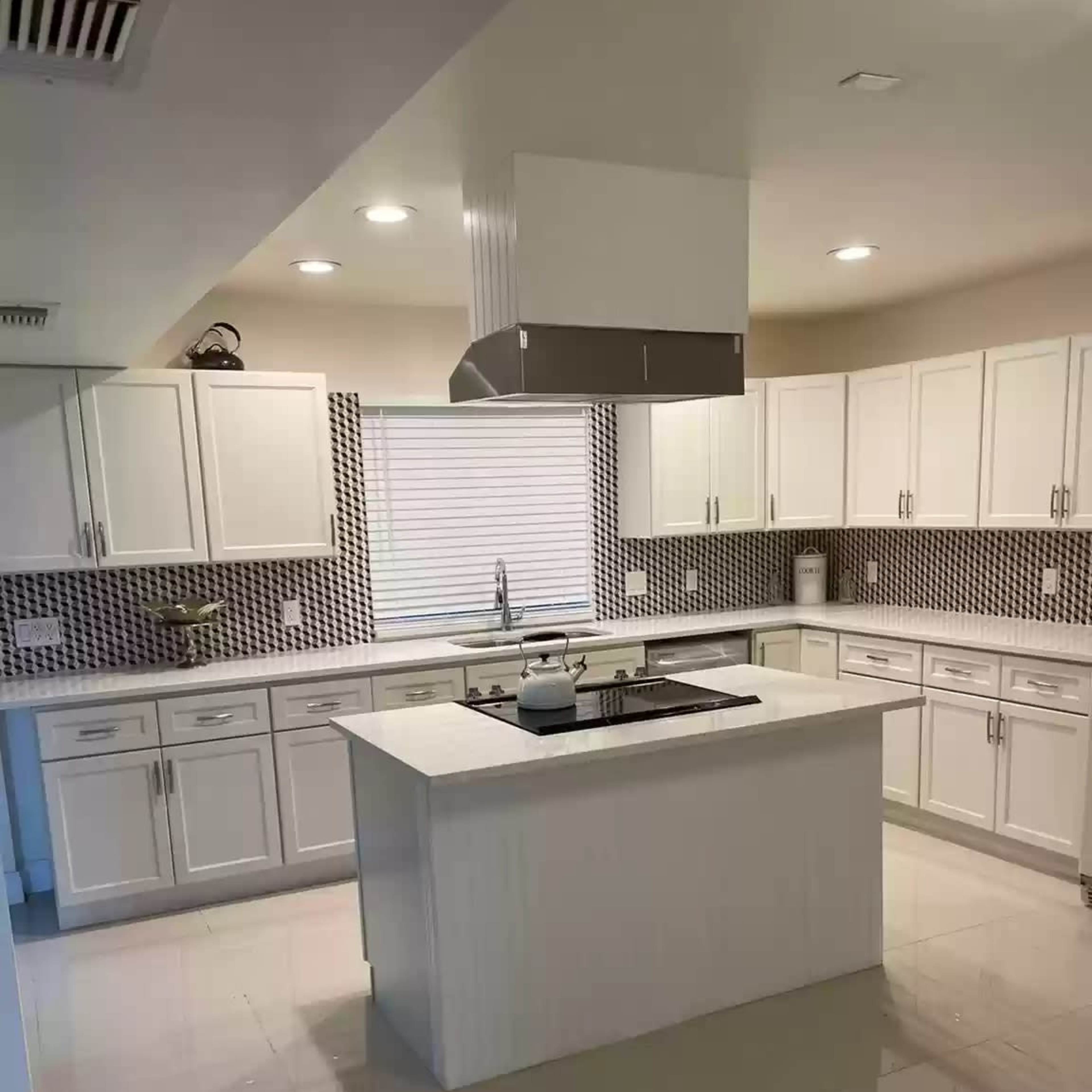 A modern kitchen with white cabinets, a central island, and a patterned backsplash.