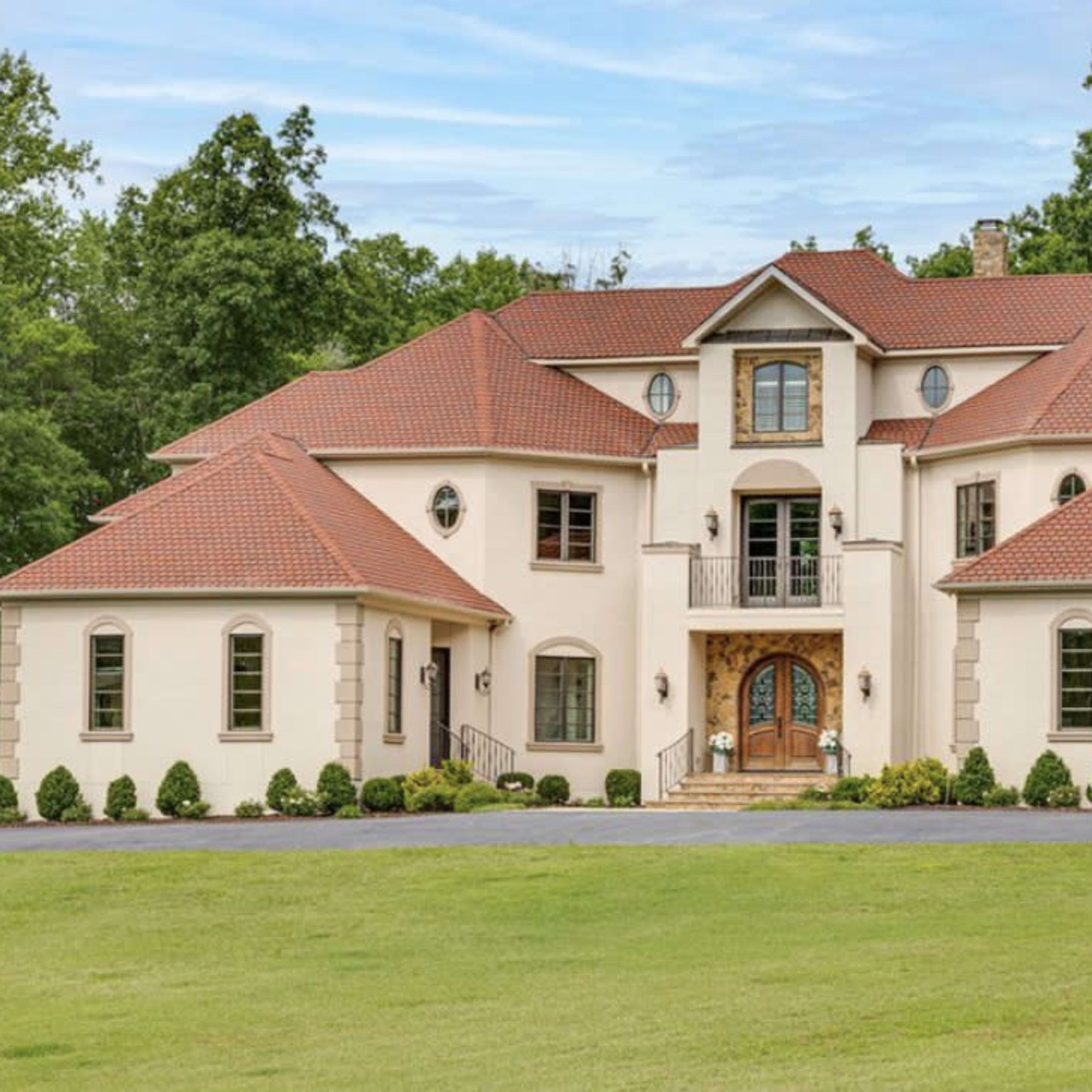 A large, two-story house with a red-tiled roof and a well-manicured lawn, surrounded by trees.