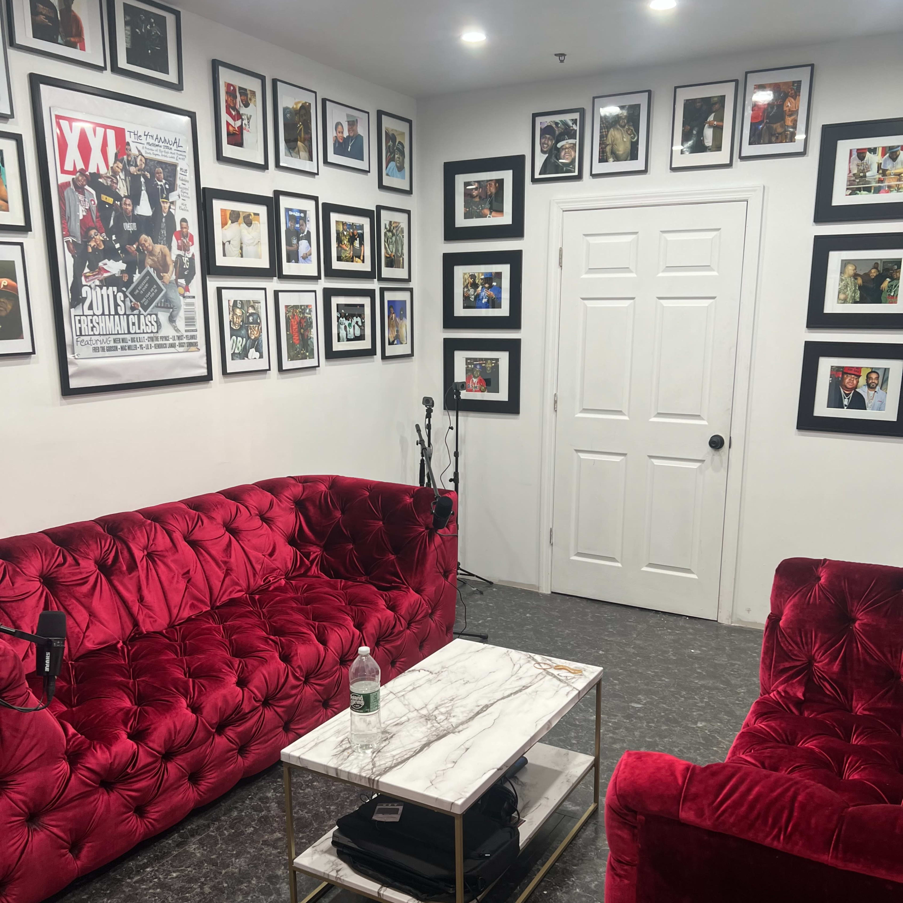 The room features two red velvet sofas facing a marble-topped coffee table, with numerous framed photographs and posters on the walls surrounding a closed white door.