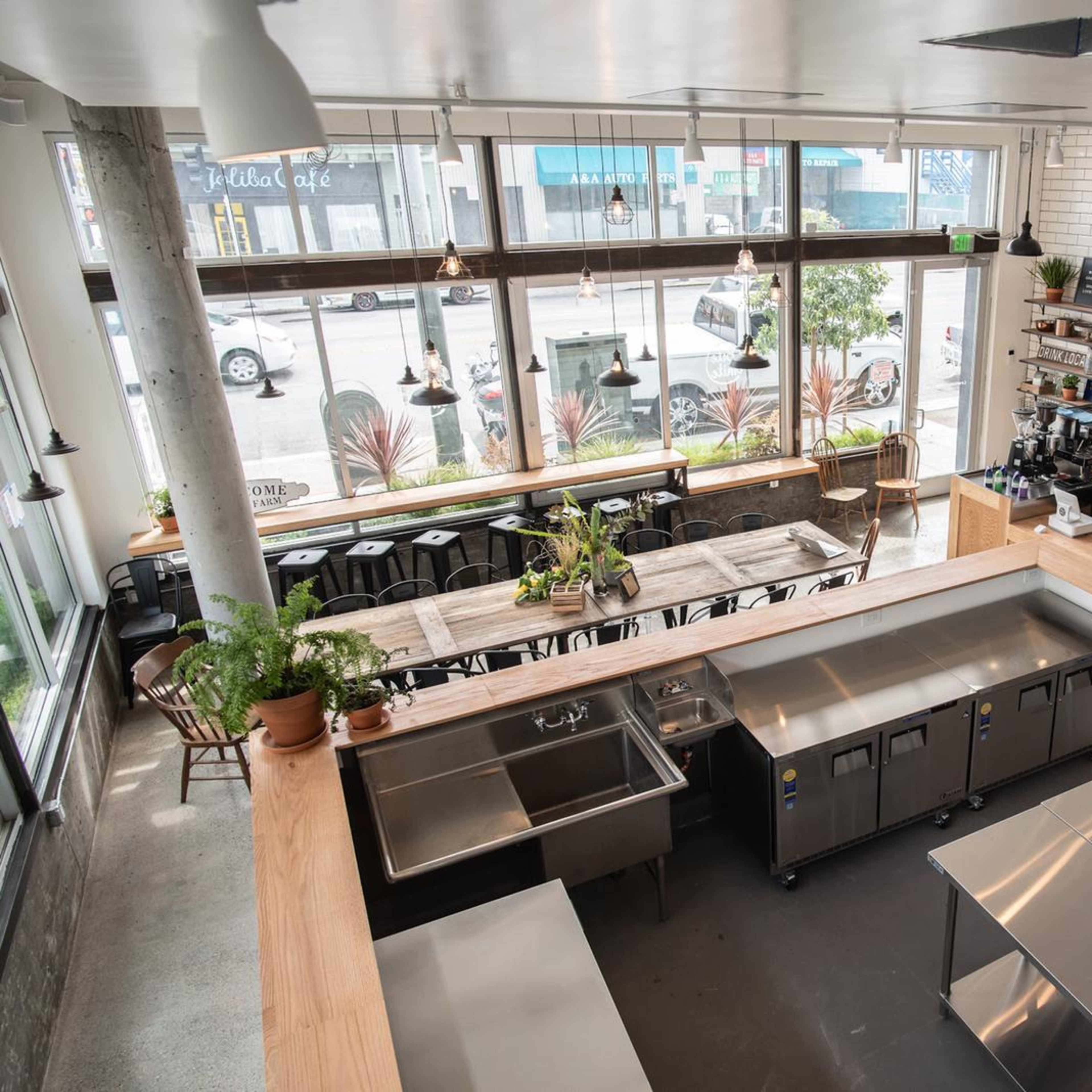 A modern café interior with large windows, wooden tables, and a stainless steel kitchen area.