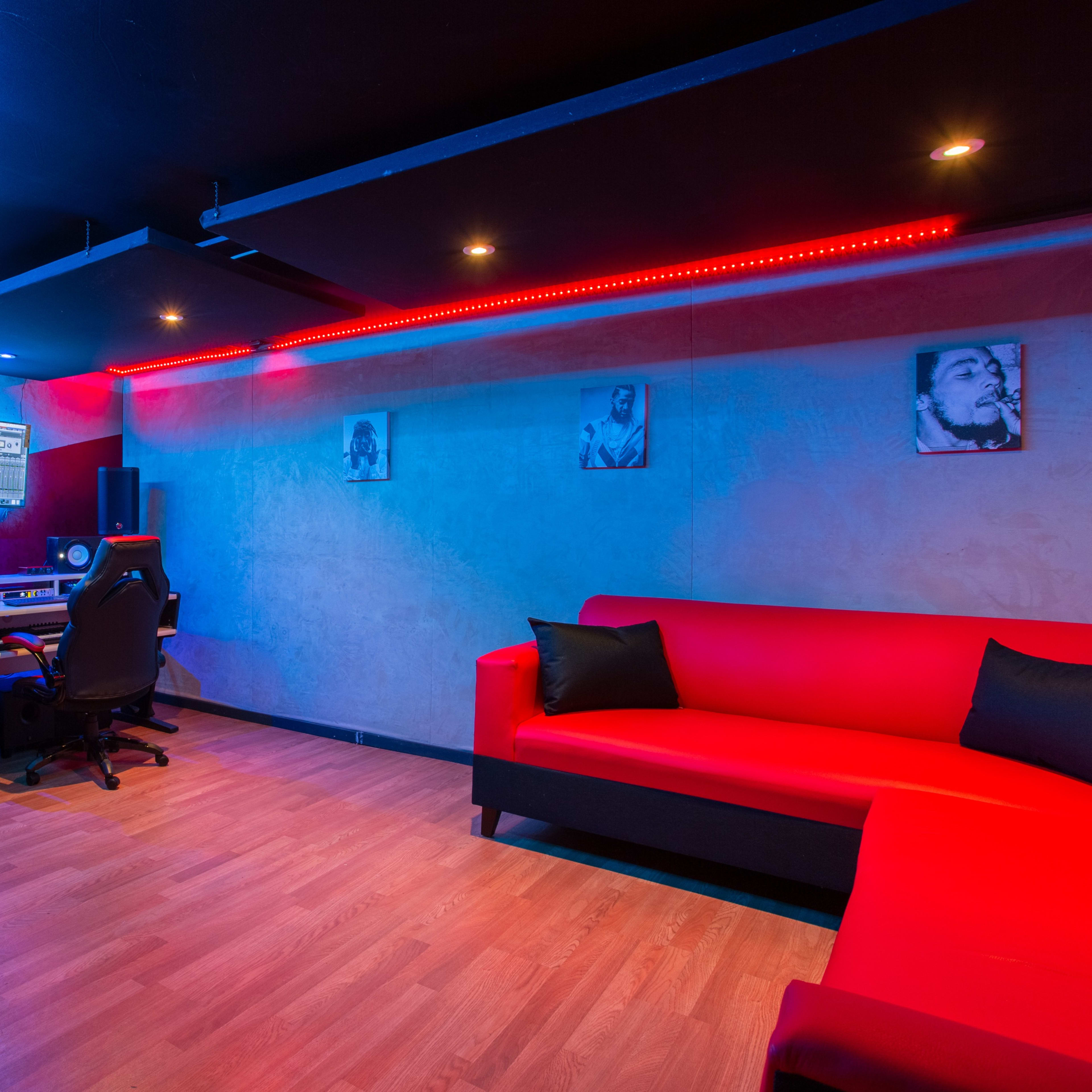 A modern recording studio features a red couch, digital equipment, and colorful lighting on the walls.
