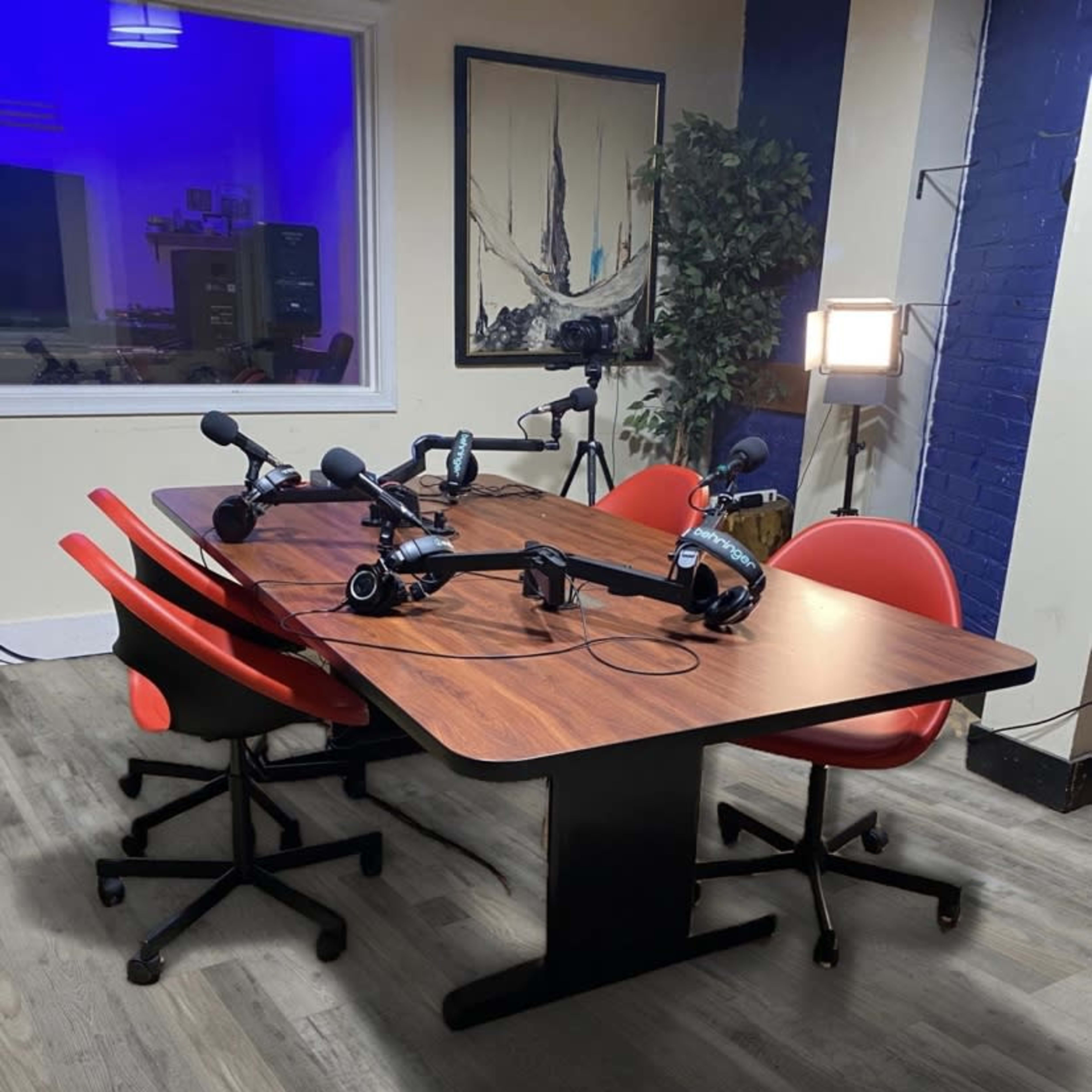 A round table with four chairs and microphones set up for a podcast recording in a brightly lit room.